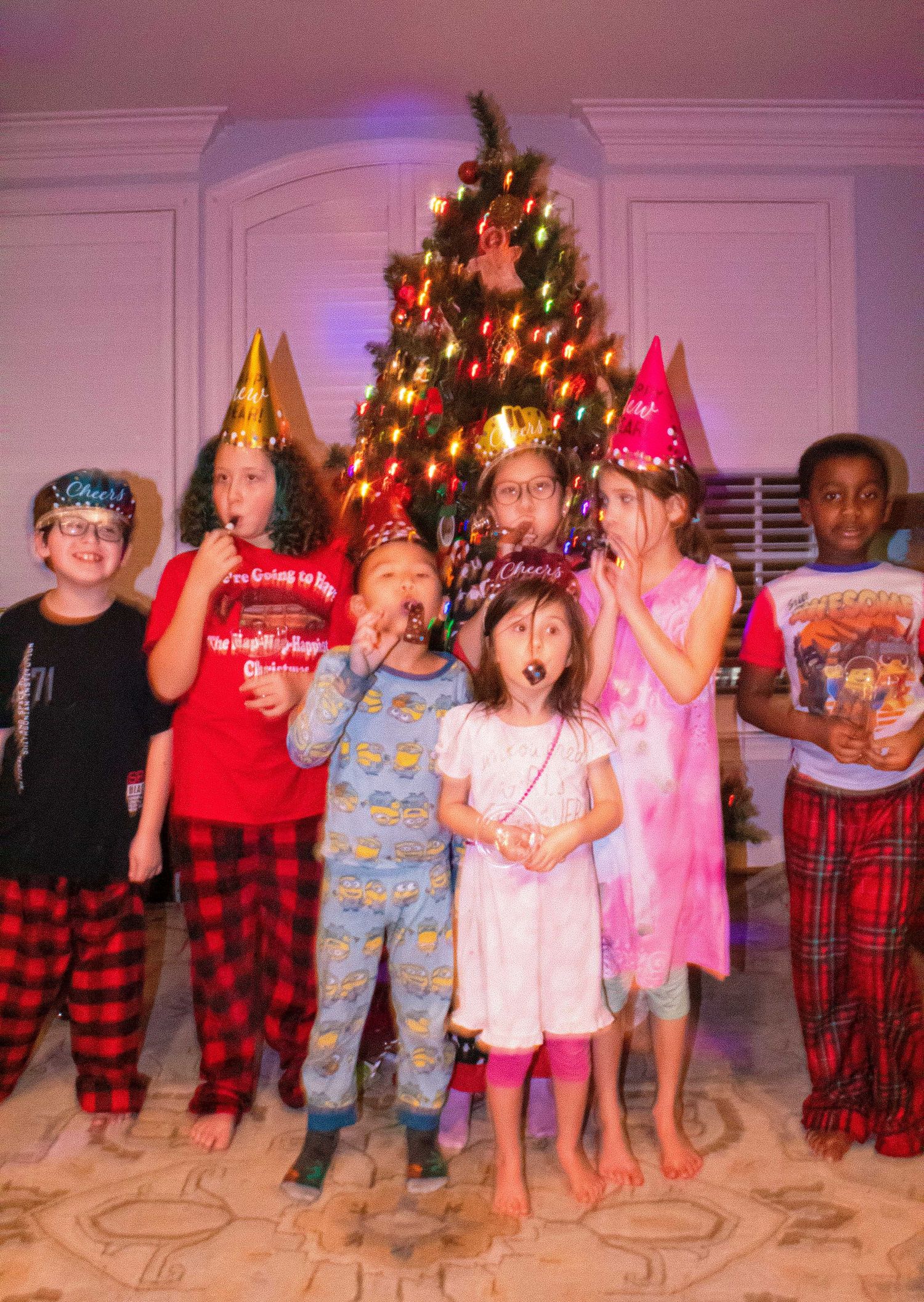 Group photo of children in pajamas posing in front of a decorated Christmas tree.