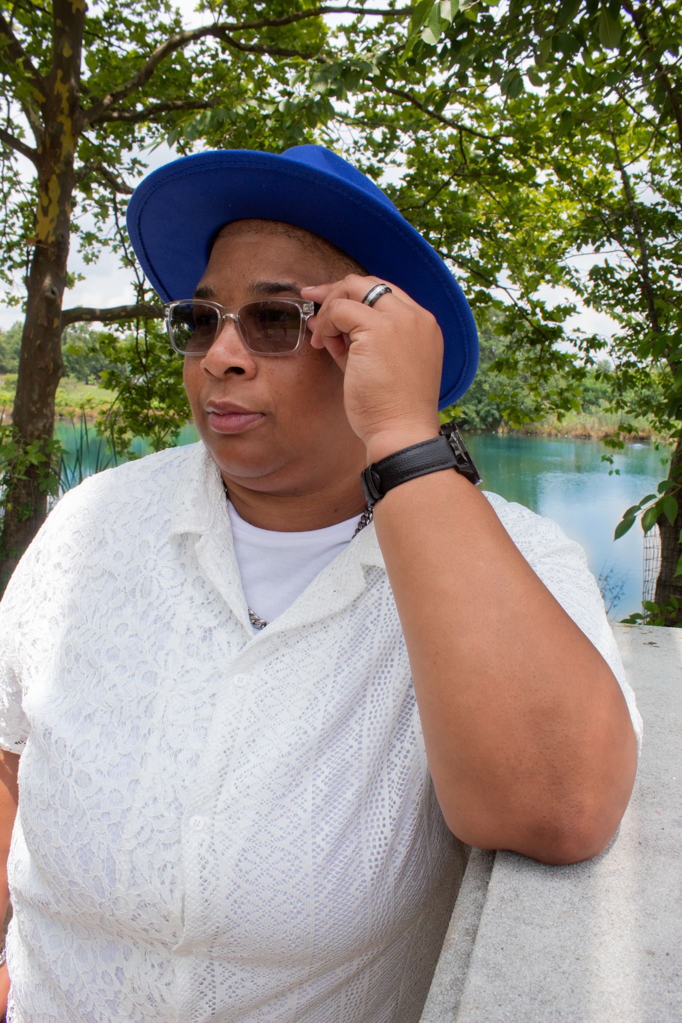 Person wearing white outfit and blue cap posing with sunglasses outdoors.