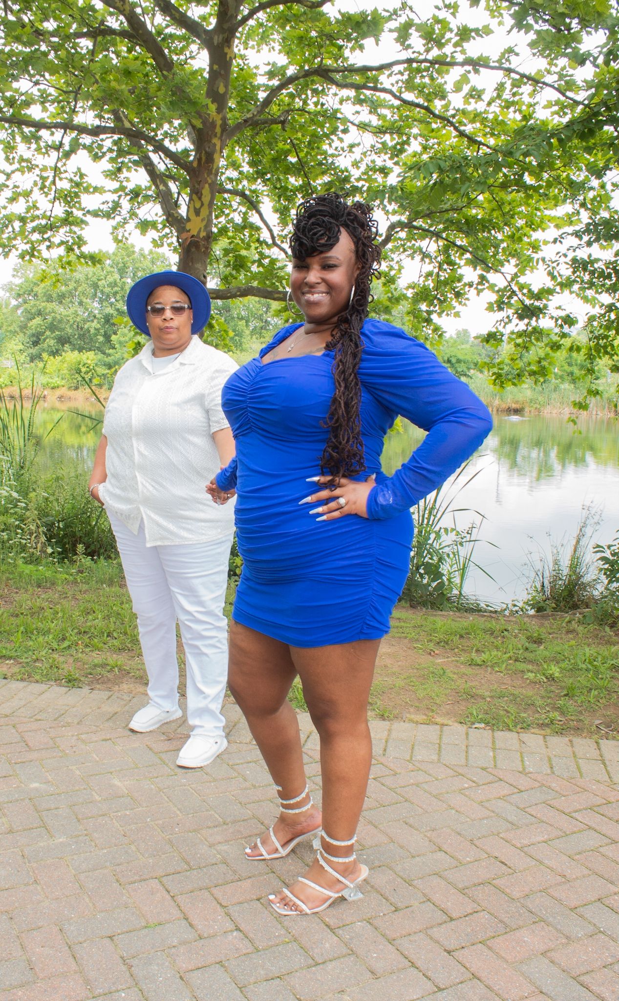Two people in blue and white outfits posing on a brick pathway with a pond visible in the background.