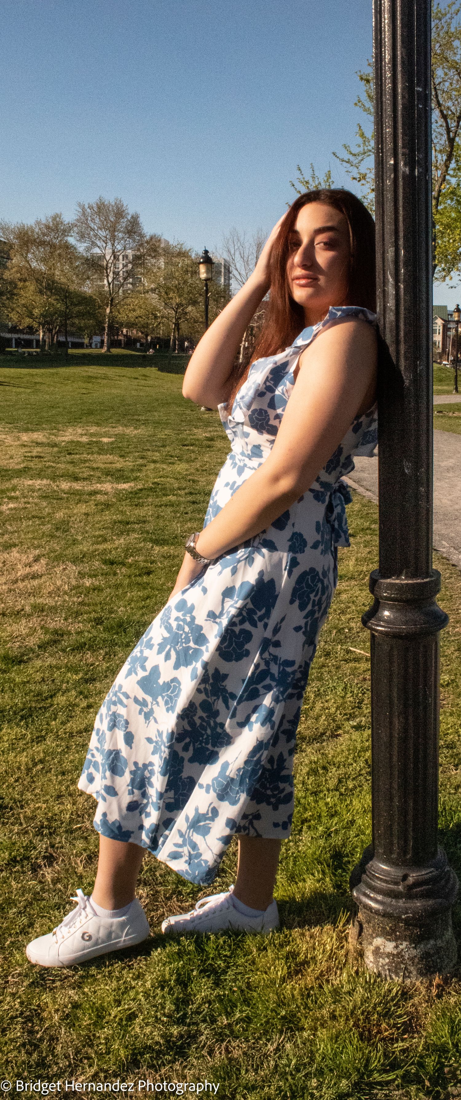 Casual outdoor portrait with a blue floral dress and white sneakers against a lamppost.