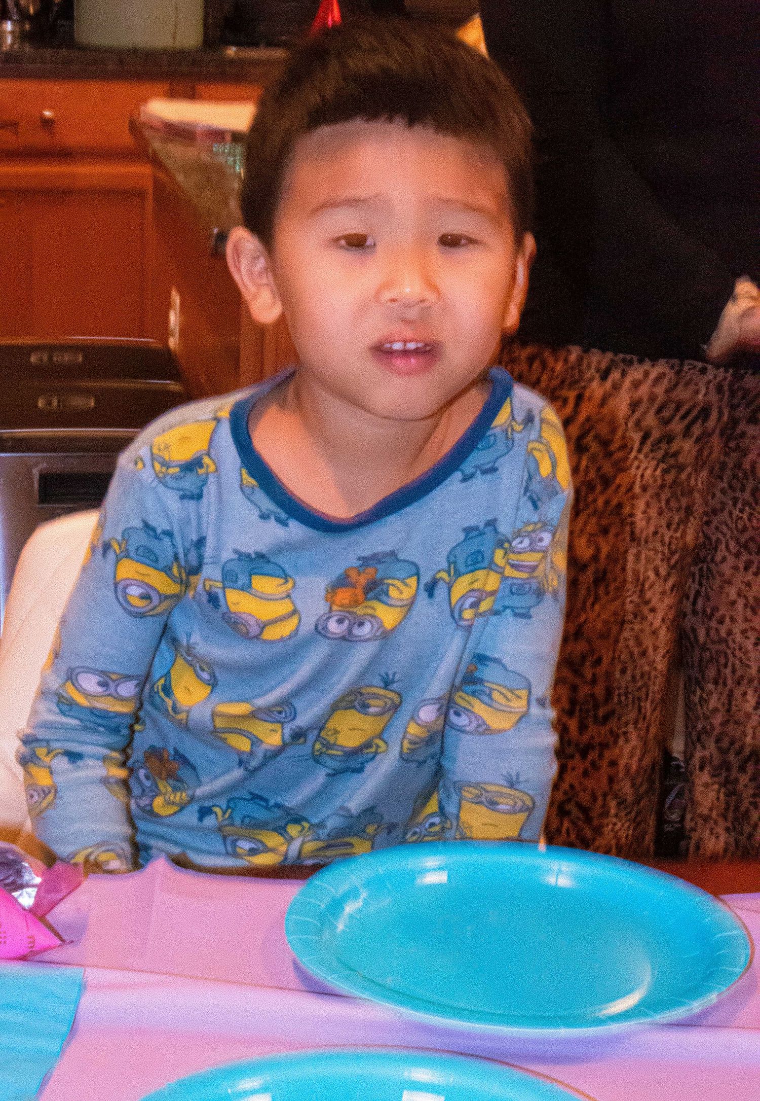 Child in blue patterned pajamas sitting at table with bright party plates.