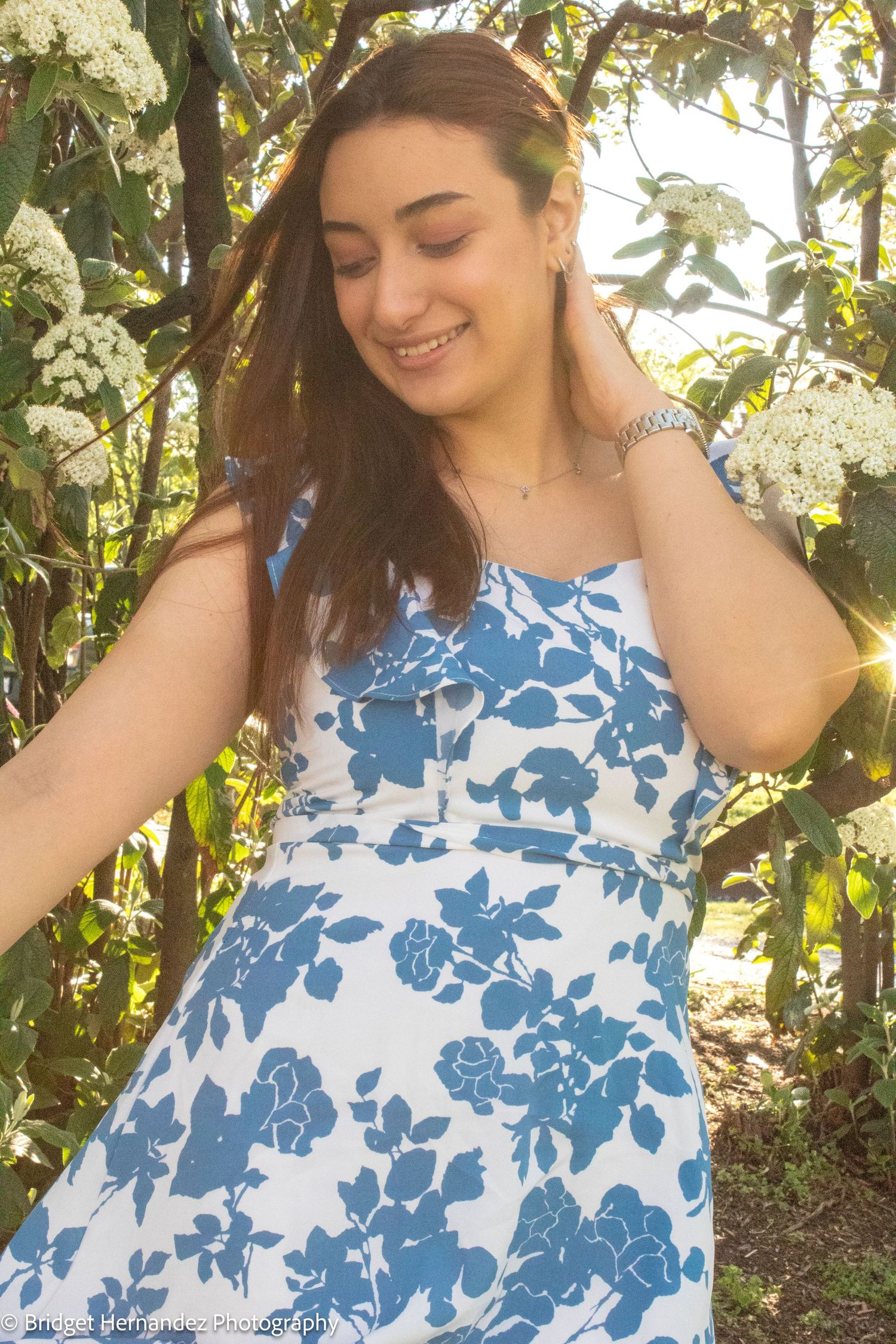 Candid garden portrait in blue floral dress among white blooming flowers.