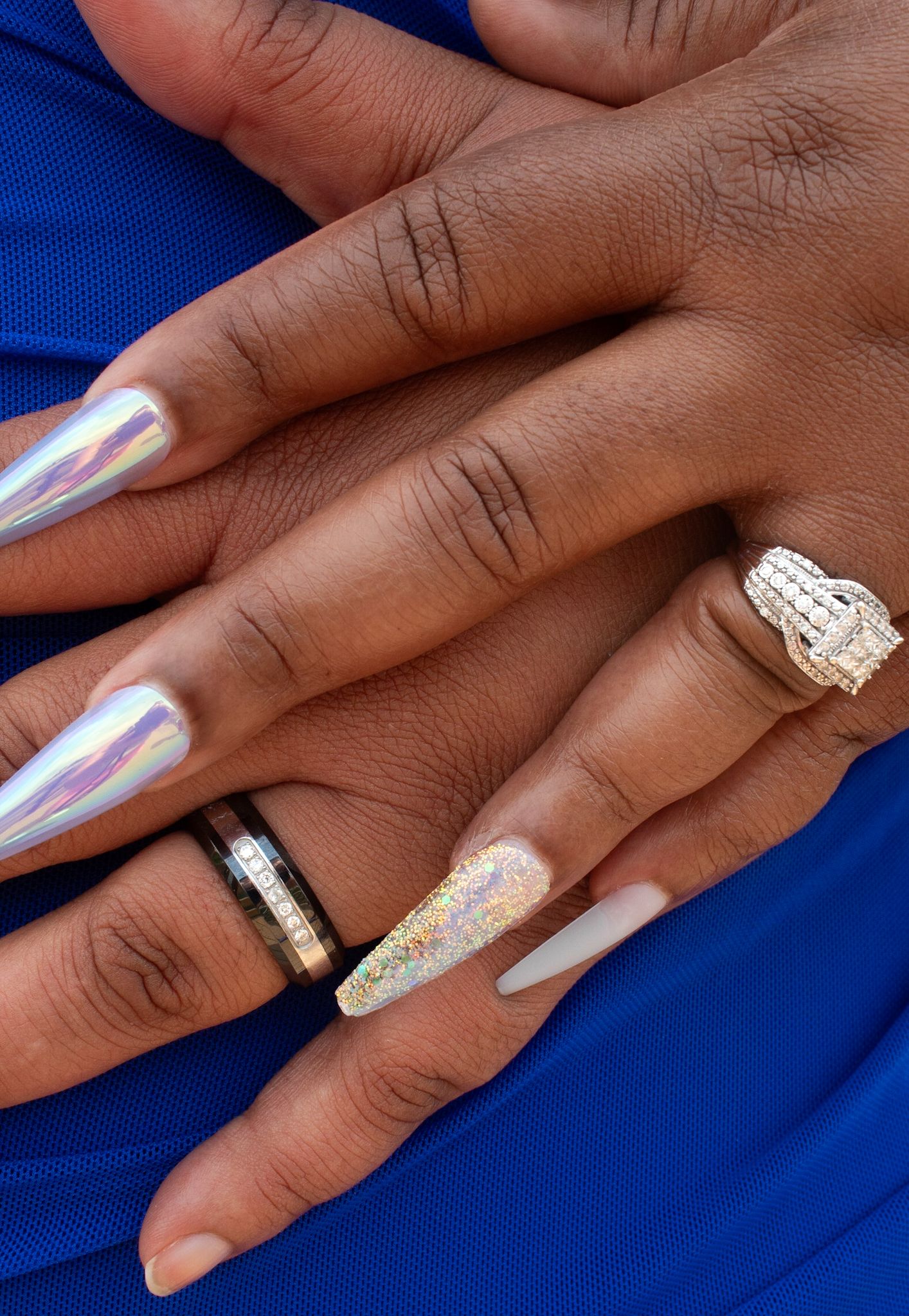Elegant engagement ring and manicured nails showcased against vibrant blue background.