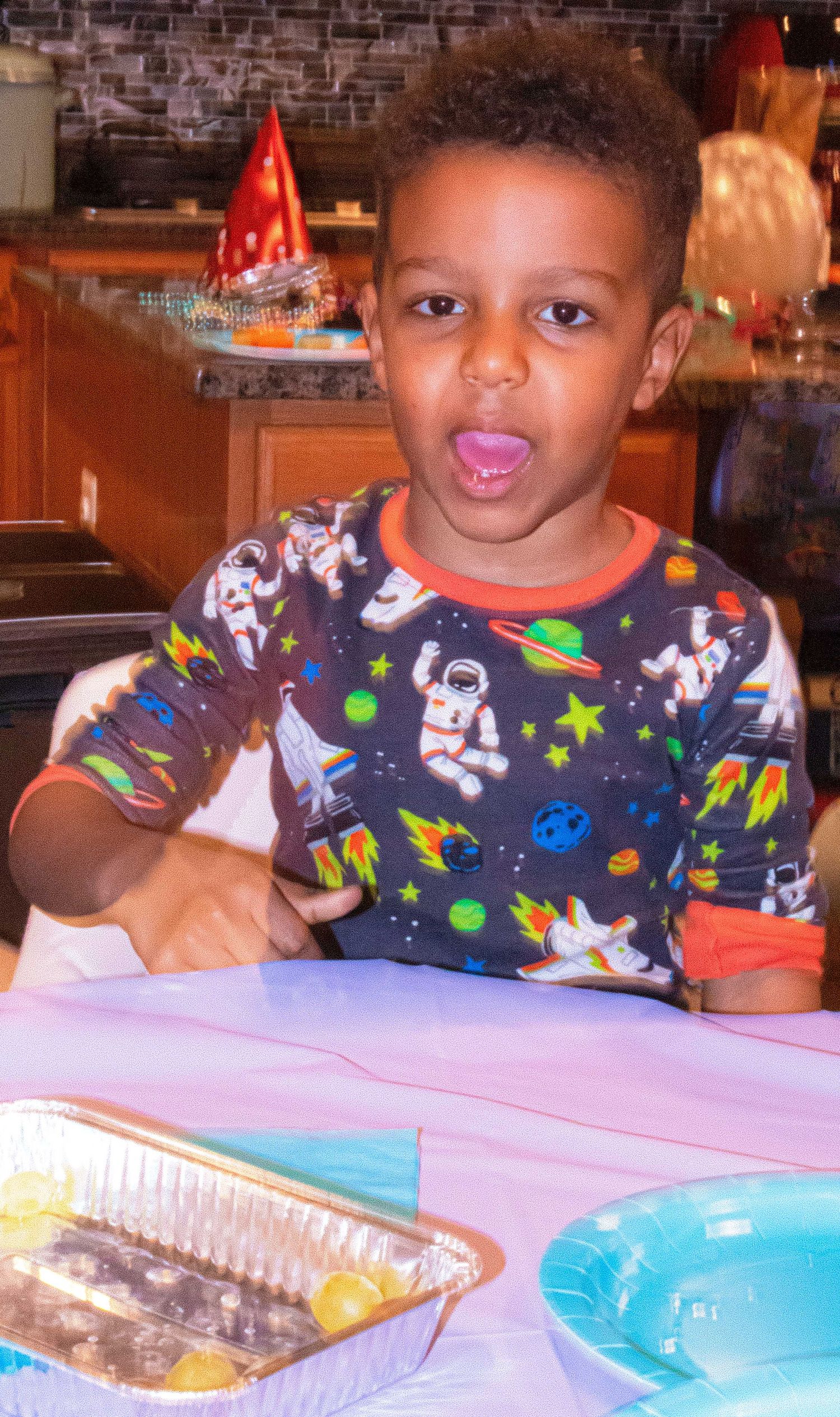 Child wearing space-themed shirt sits at party table with blue and pink decorations.