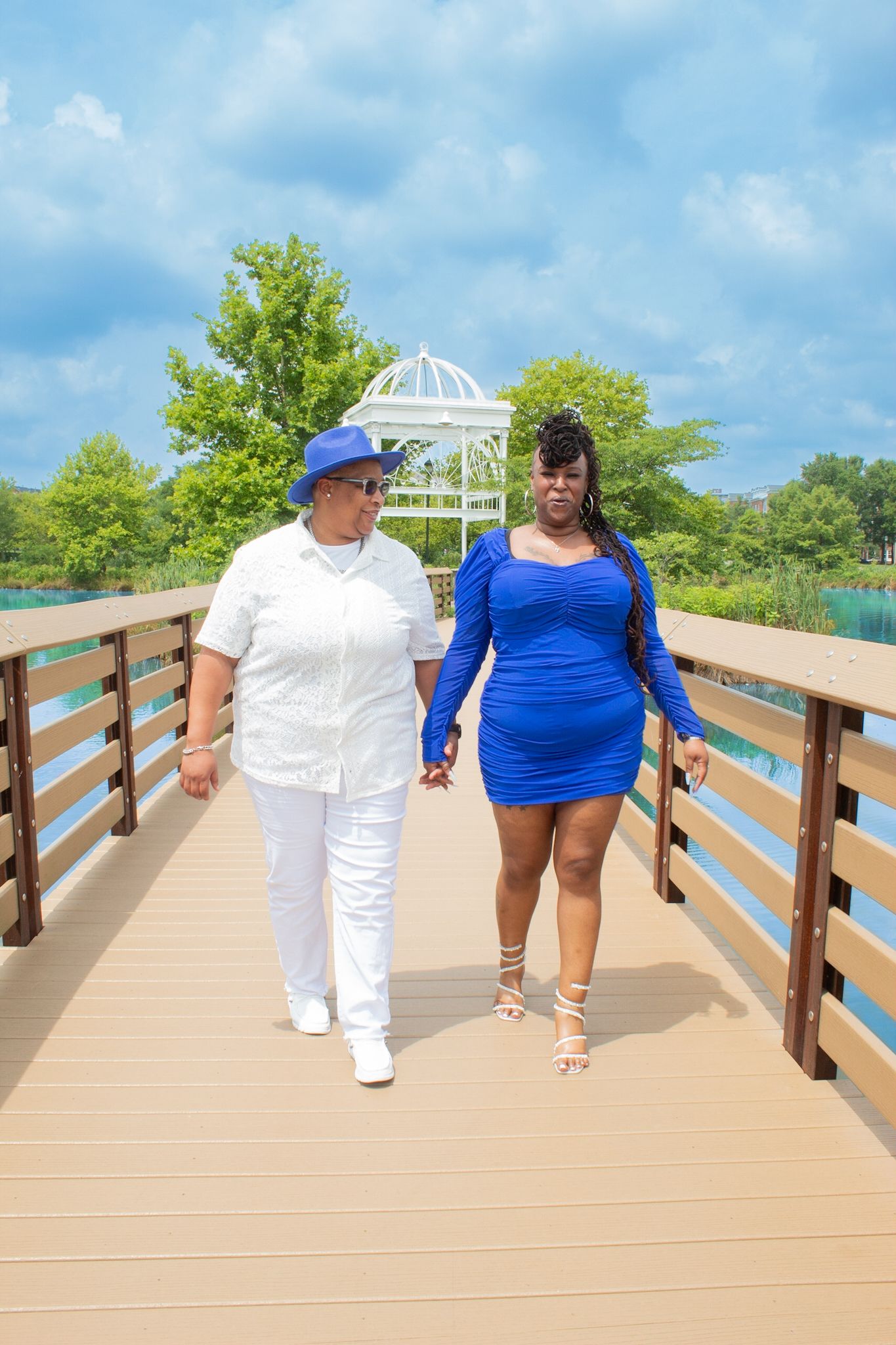 Two people stroll hand in hand along wooden boardwalk overlooking turquoise waters.