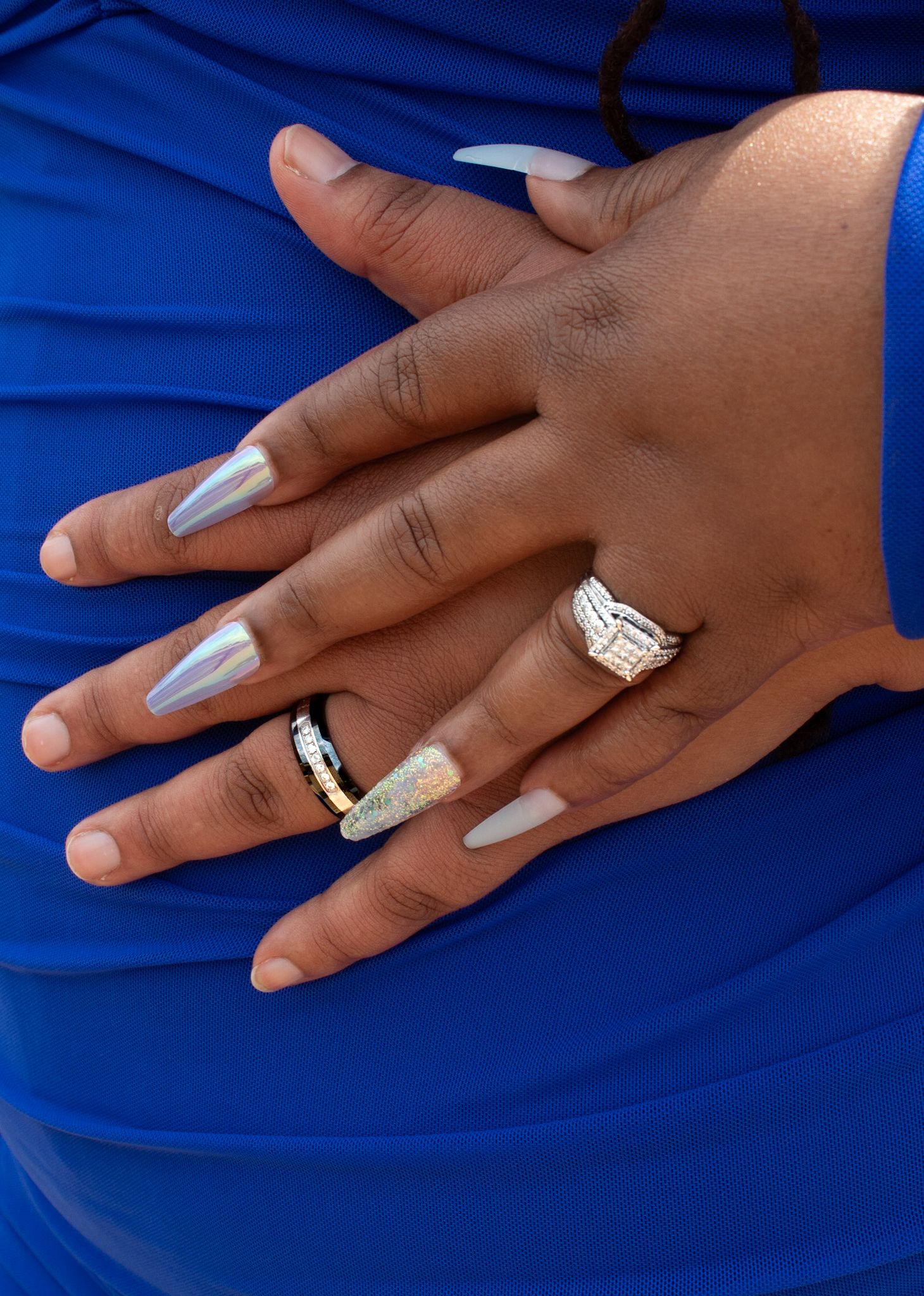 Close-up of hands with silver manicure and engagement ring against blue fabric.