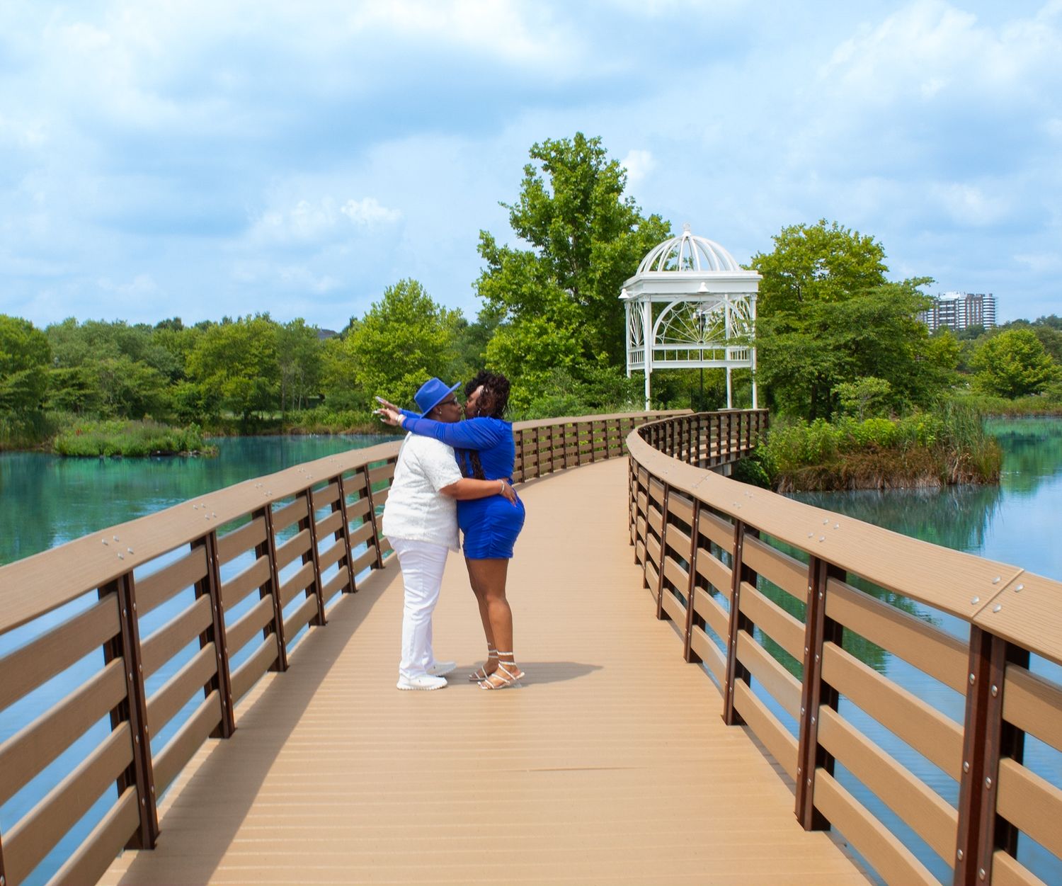 Long wooden pier extends over calm blue waters surrounded by lush greenery under bright skies.