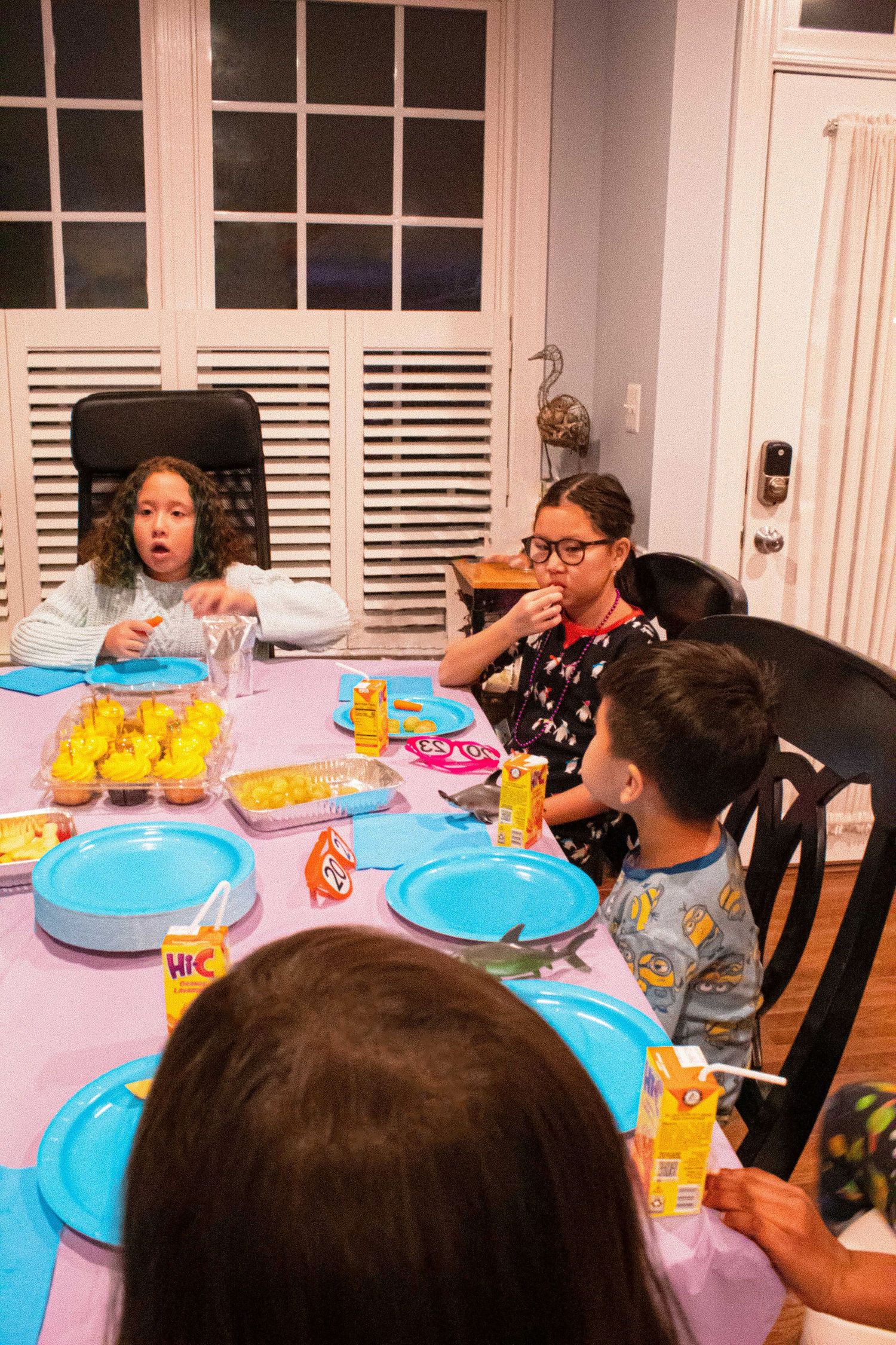 A festive gathering around a pink table with blue plates and yellow drinks.