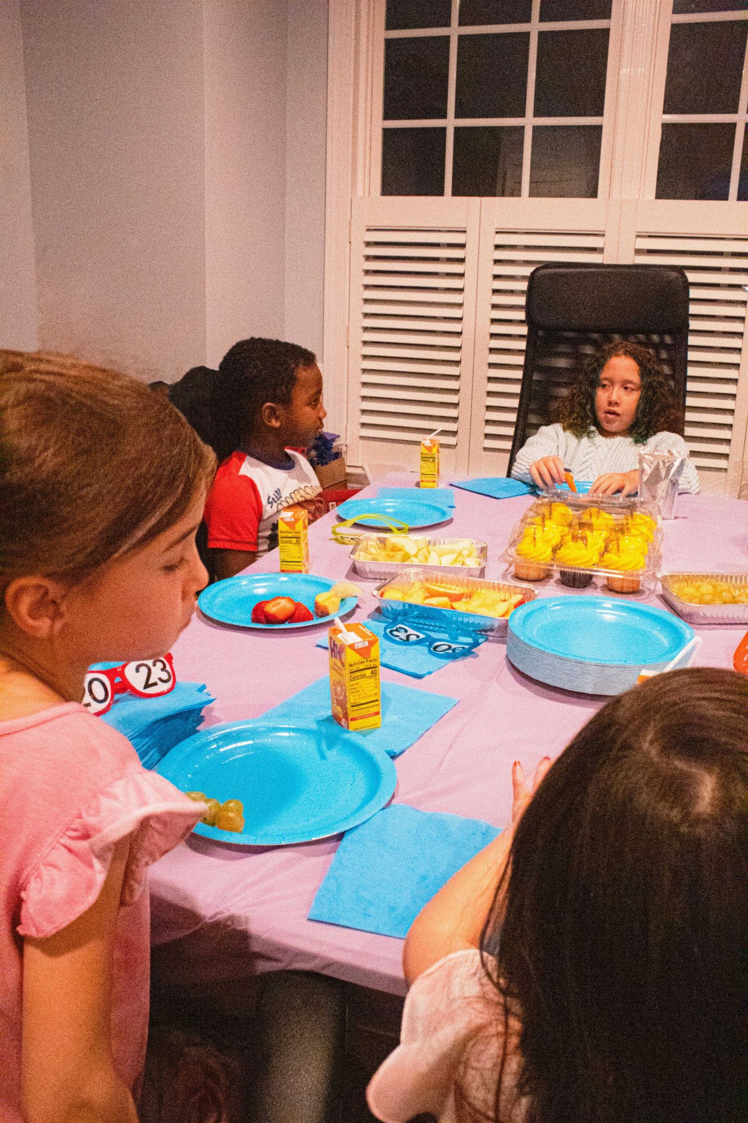 Kids seated at a pink-covered table with bright blue plates and snacks enjoying a celebration.