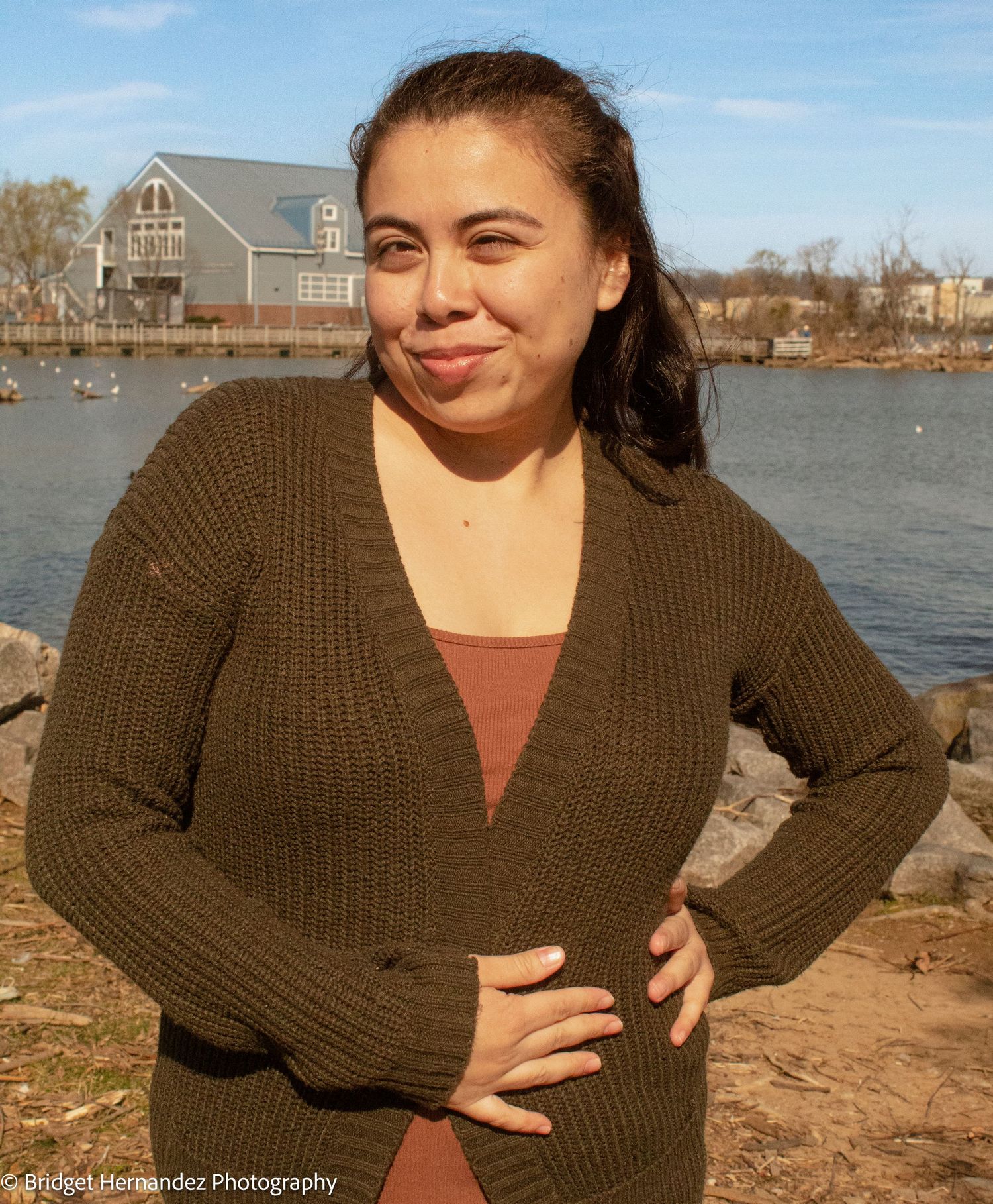 Waterfront photo series in olive knit sweater with houses and boats in background.