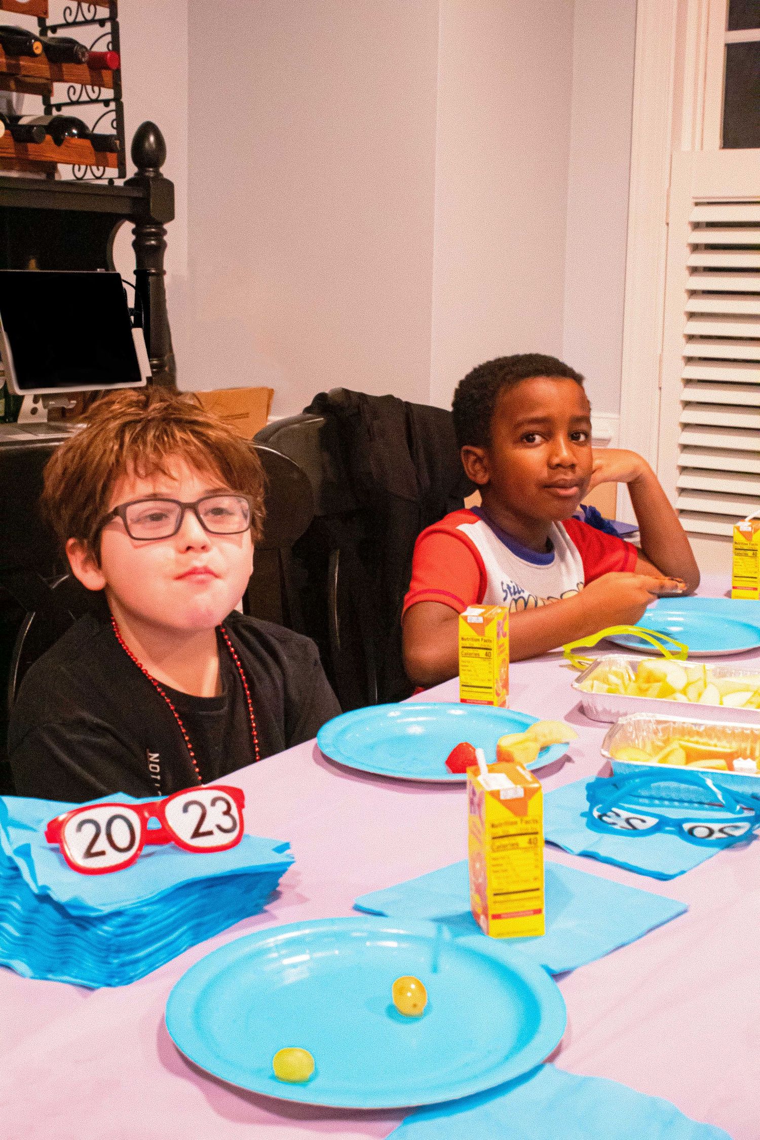 Children sitting at a party table with blue plates and yellow drinks.