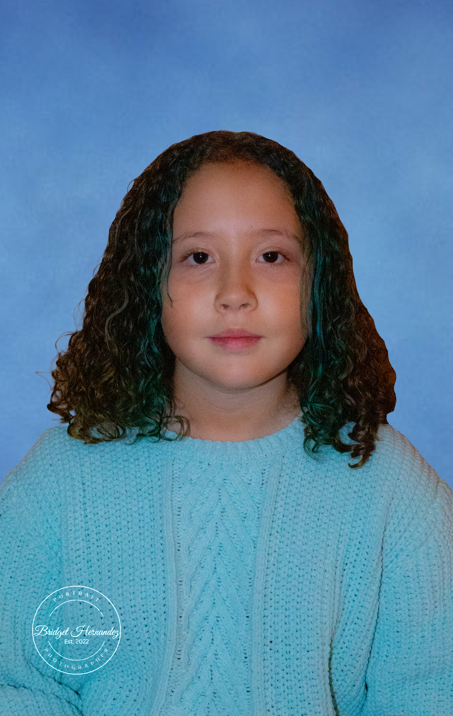 Child wearing a light blue cable knit sweater photographed against a blue background.