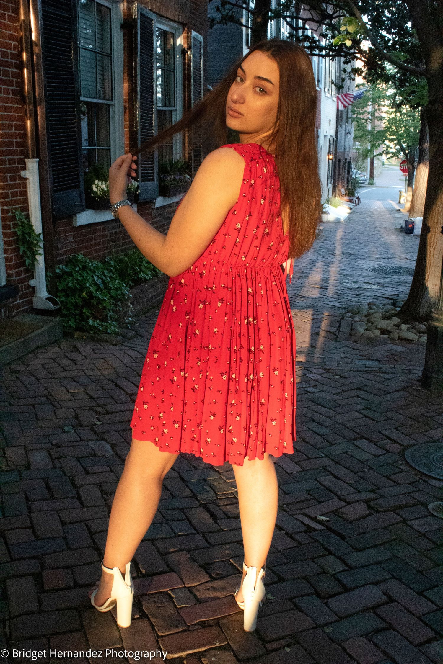 Red summer dress captured against historic brick architecture at dusk.