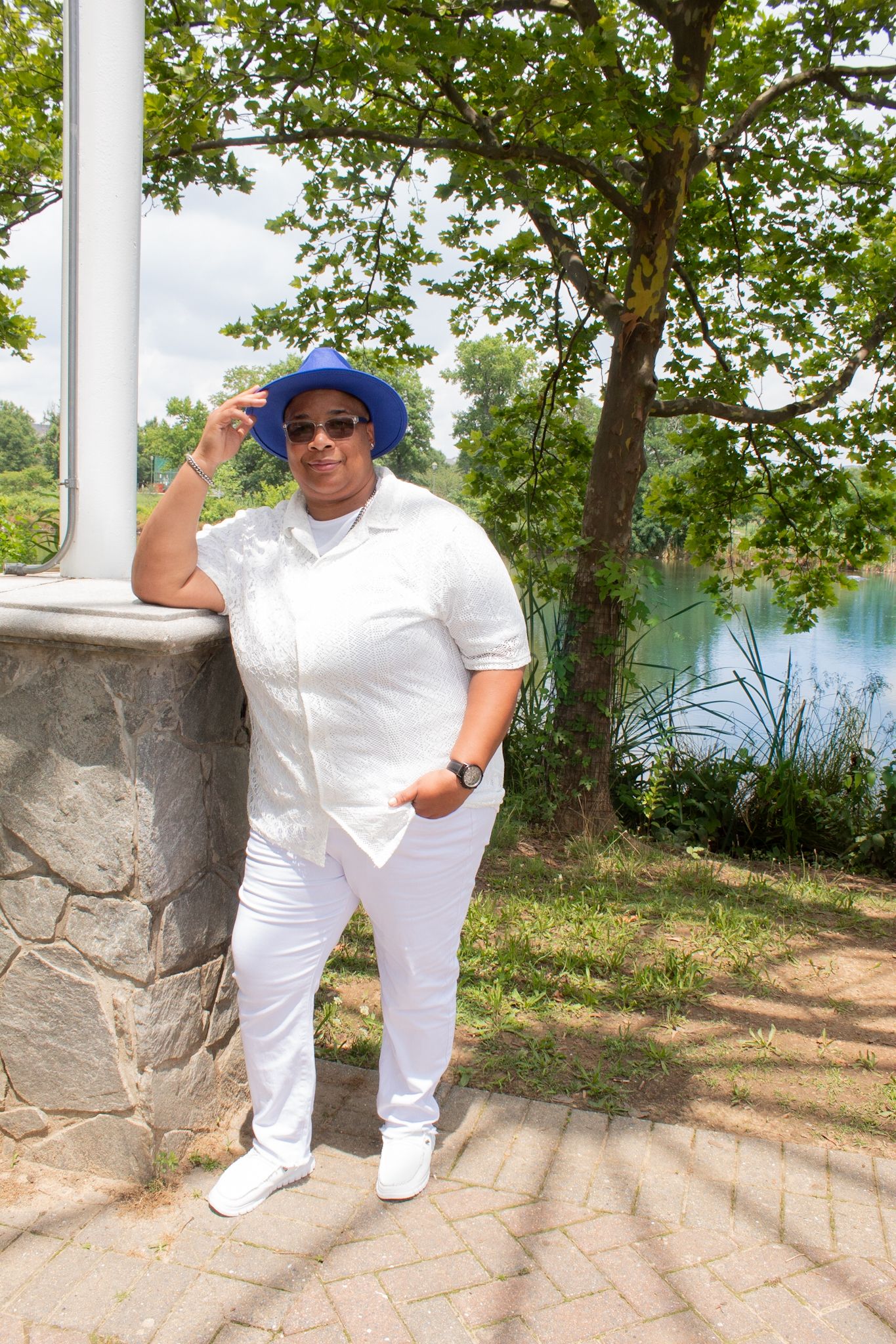 Figure in all white attire striking poses on a stone walkway with a lake backdrop.