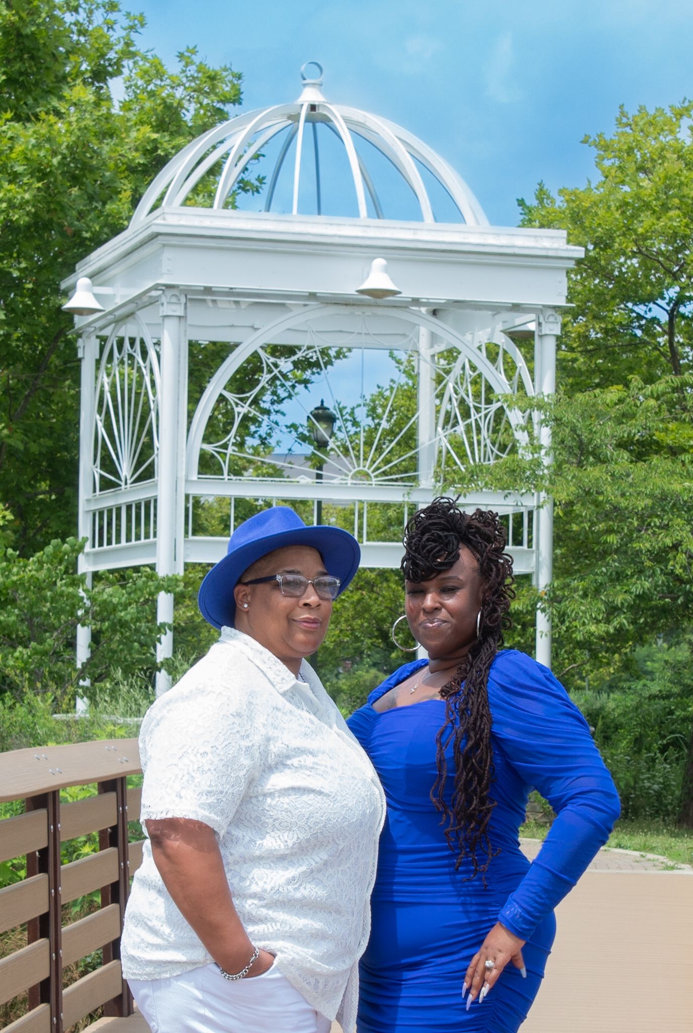 Two people share a moment near an ornate white gazebo on a waterfront boardwalk.