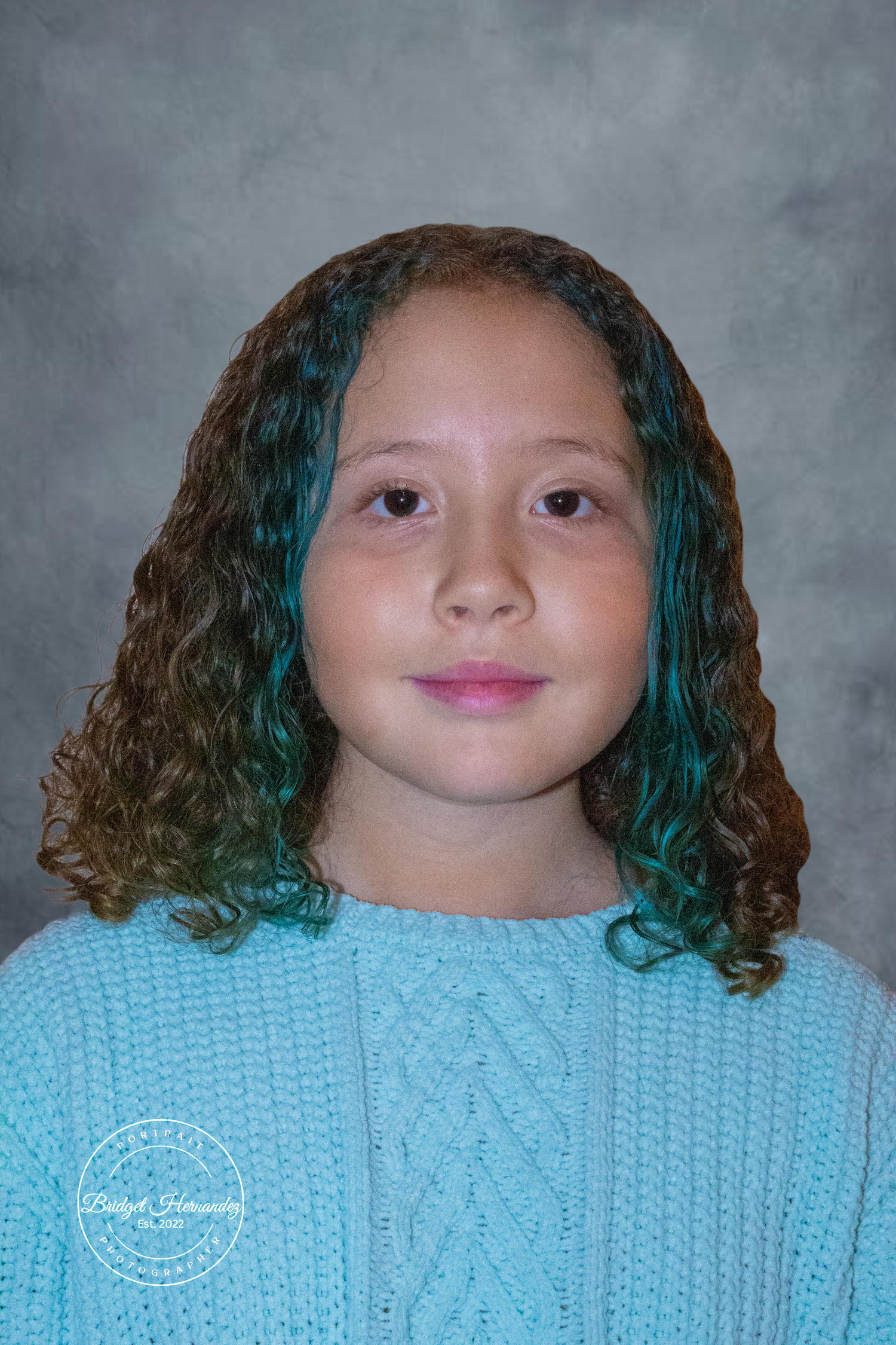 Person in light blue sweater with blue streaks in their hair against gray background.