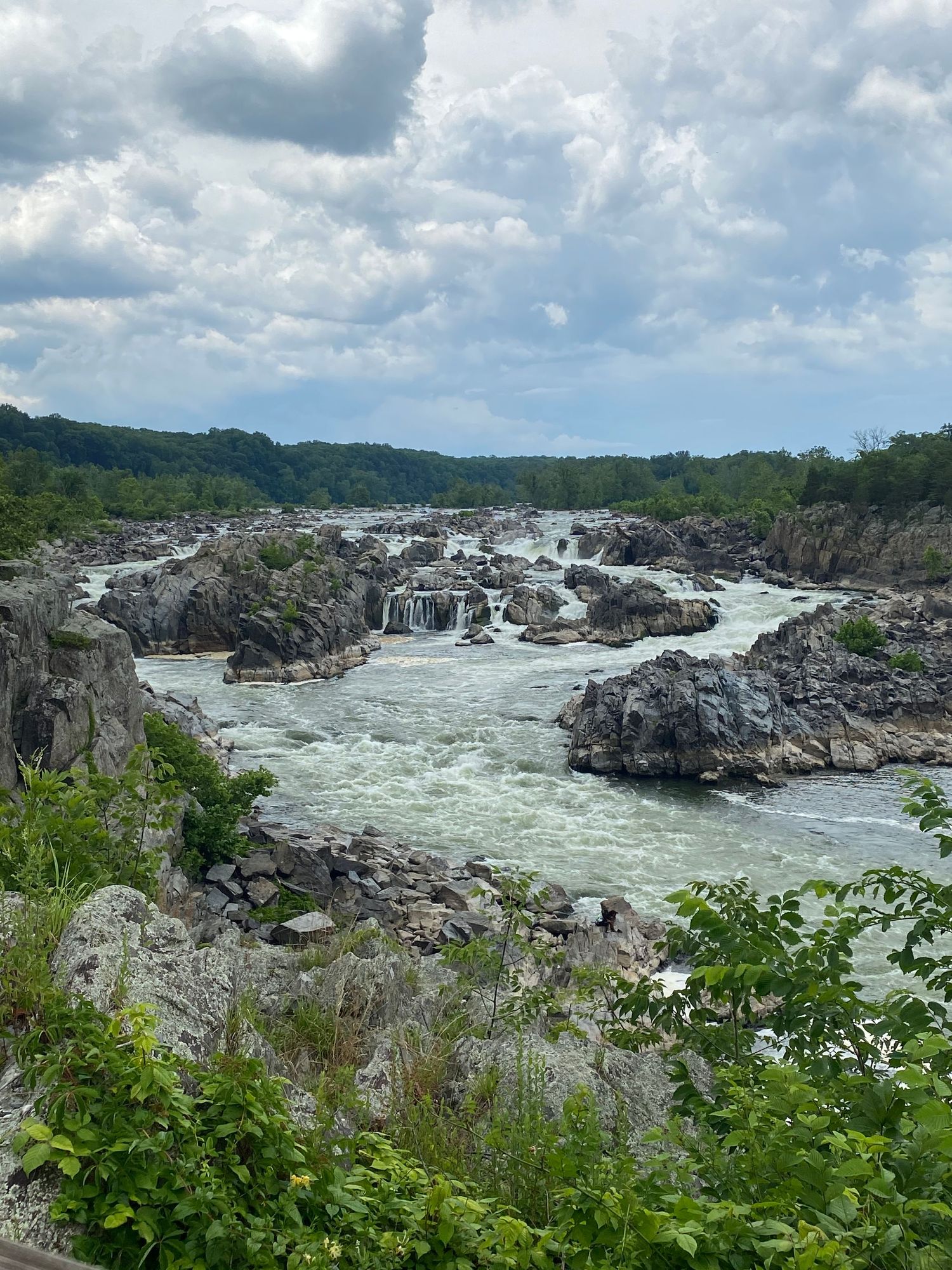 Rocky rapids and white water flowing through Great Falls on the Potomac River with cloudy sky.