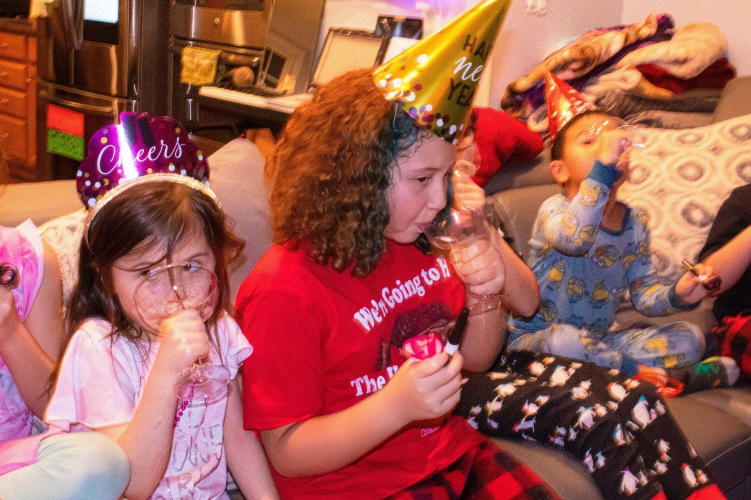 Group of kids wearing party hats and casual clothes gather at a celebration.