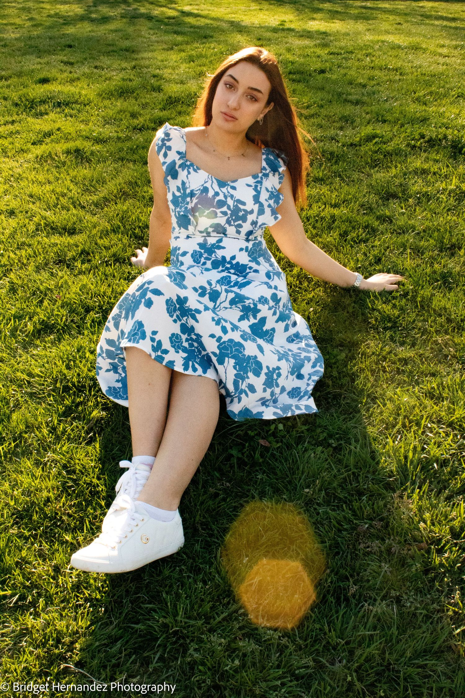 Sunny outdoor photoshoot on green grass featuring a blue and white floral dress.