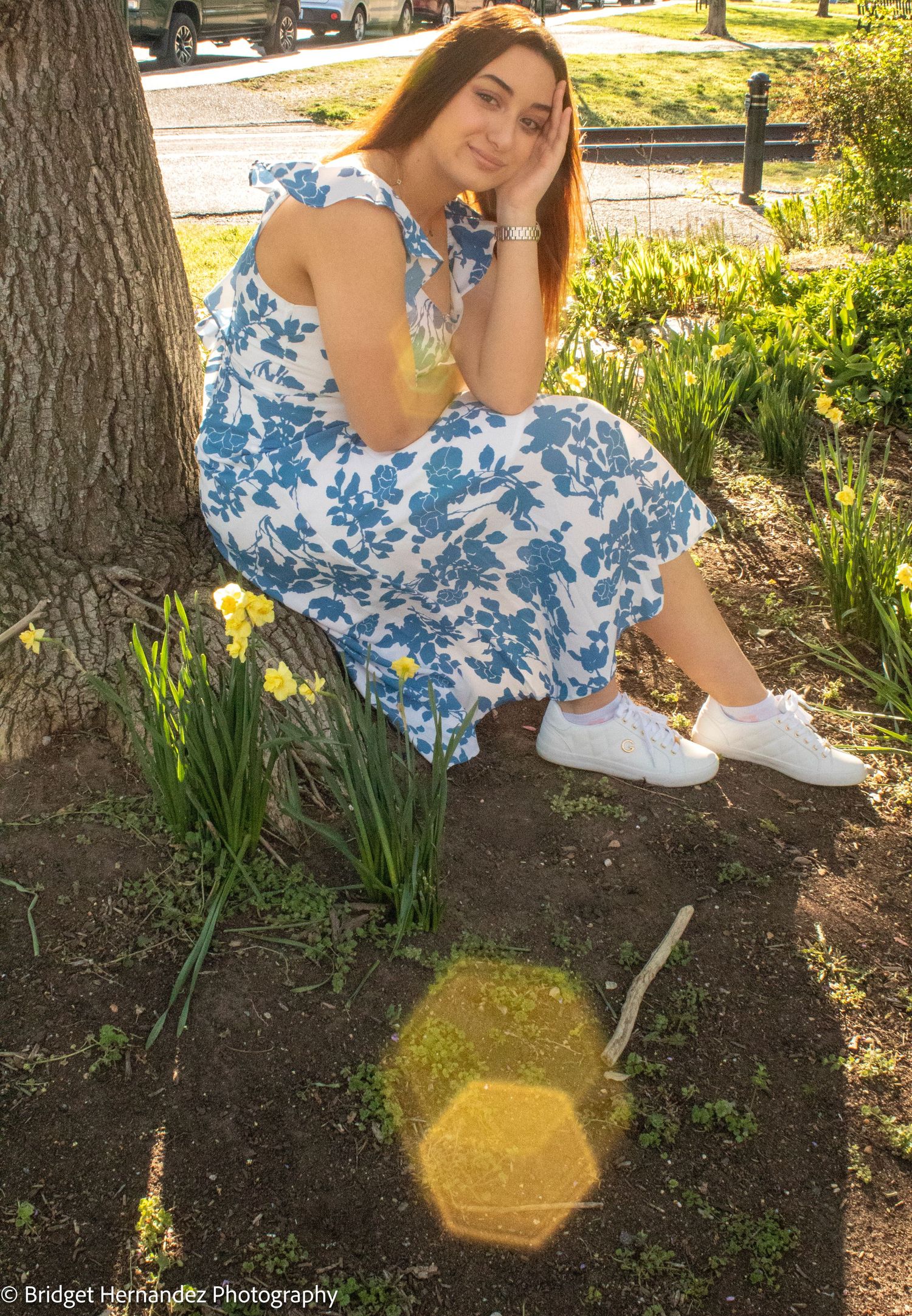 Fashion portrait crouching by tree with daffodils in foreground.