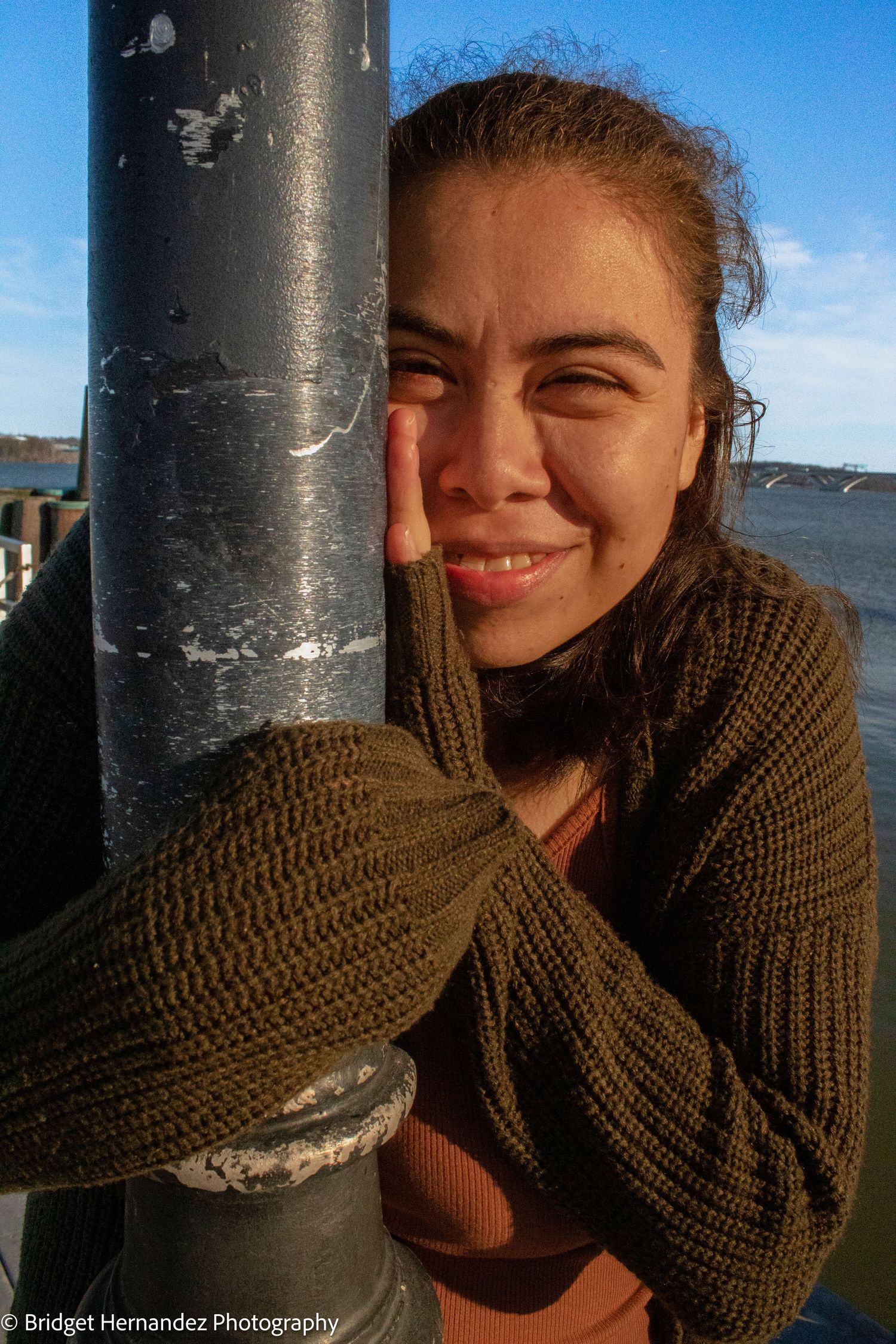Candid photo series showing playful poses against a metal pole by the water.