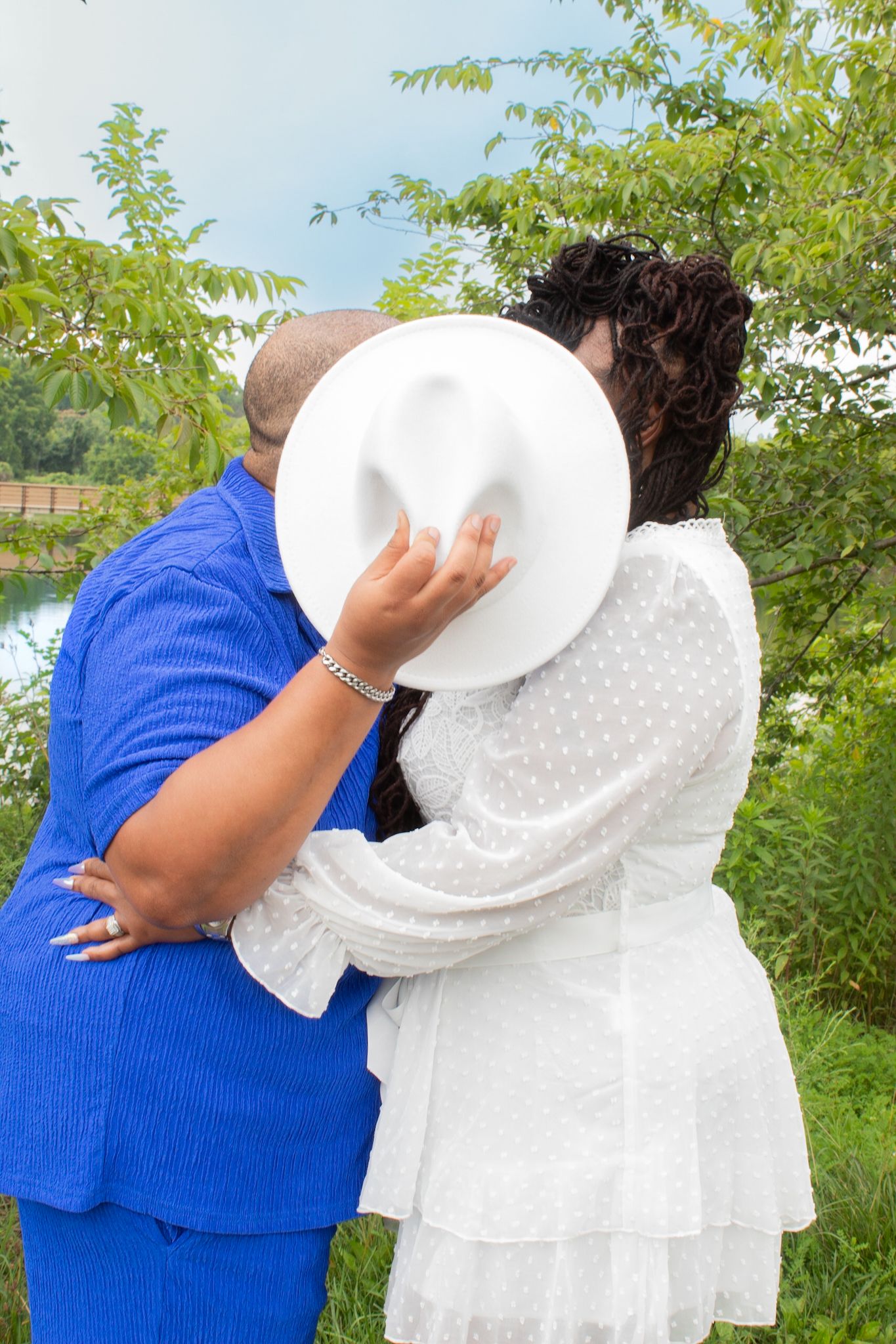 Loving embrace between couple in blue and white against natural backdrop.