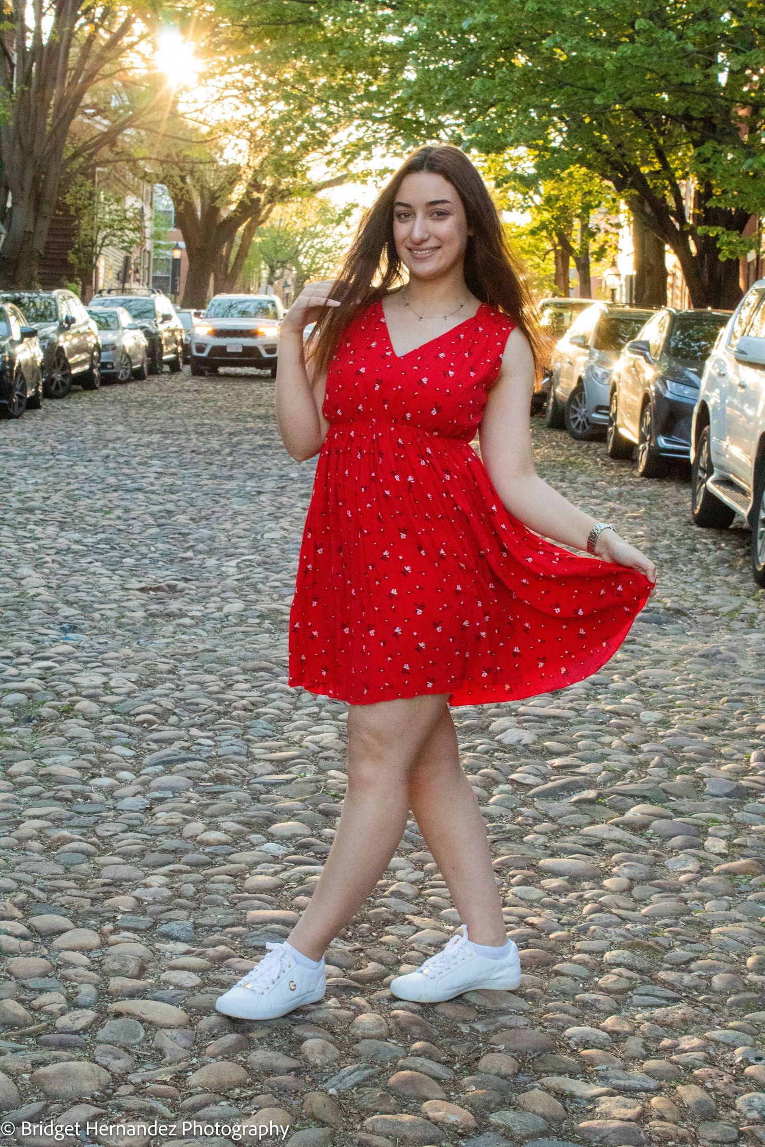 Dancing and twirling on cobblestone street in red polka dot dress and white sneakers.