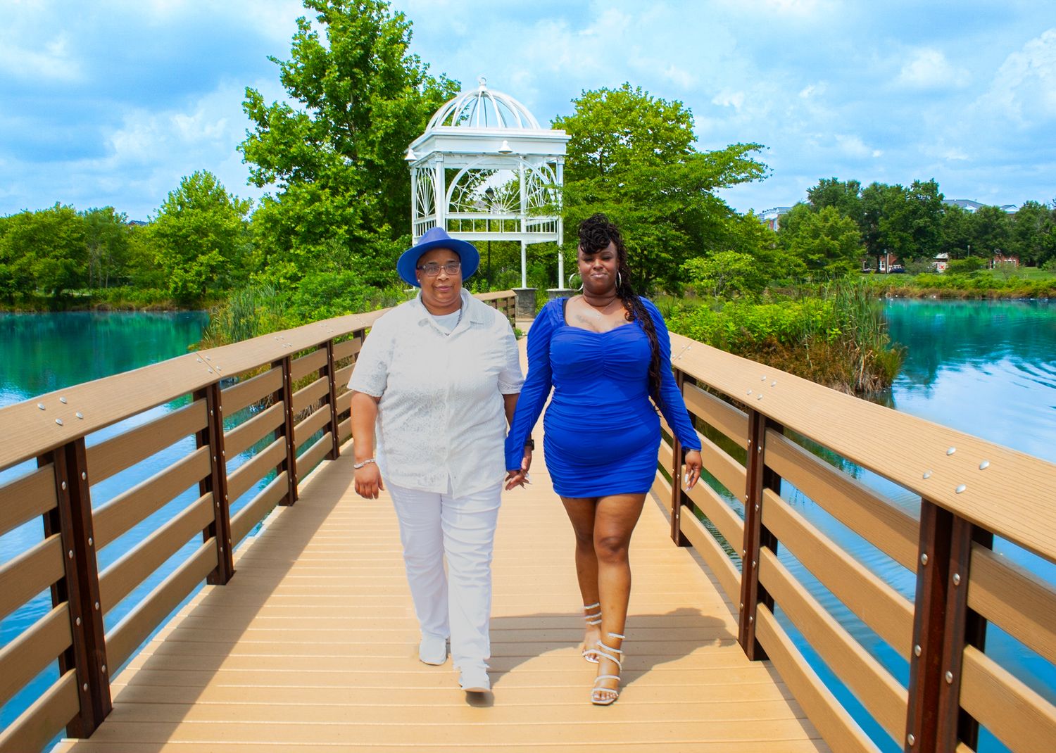 Wooden boardwalk stretches along waterfront with couple walking near white gazebo.