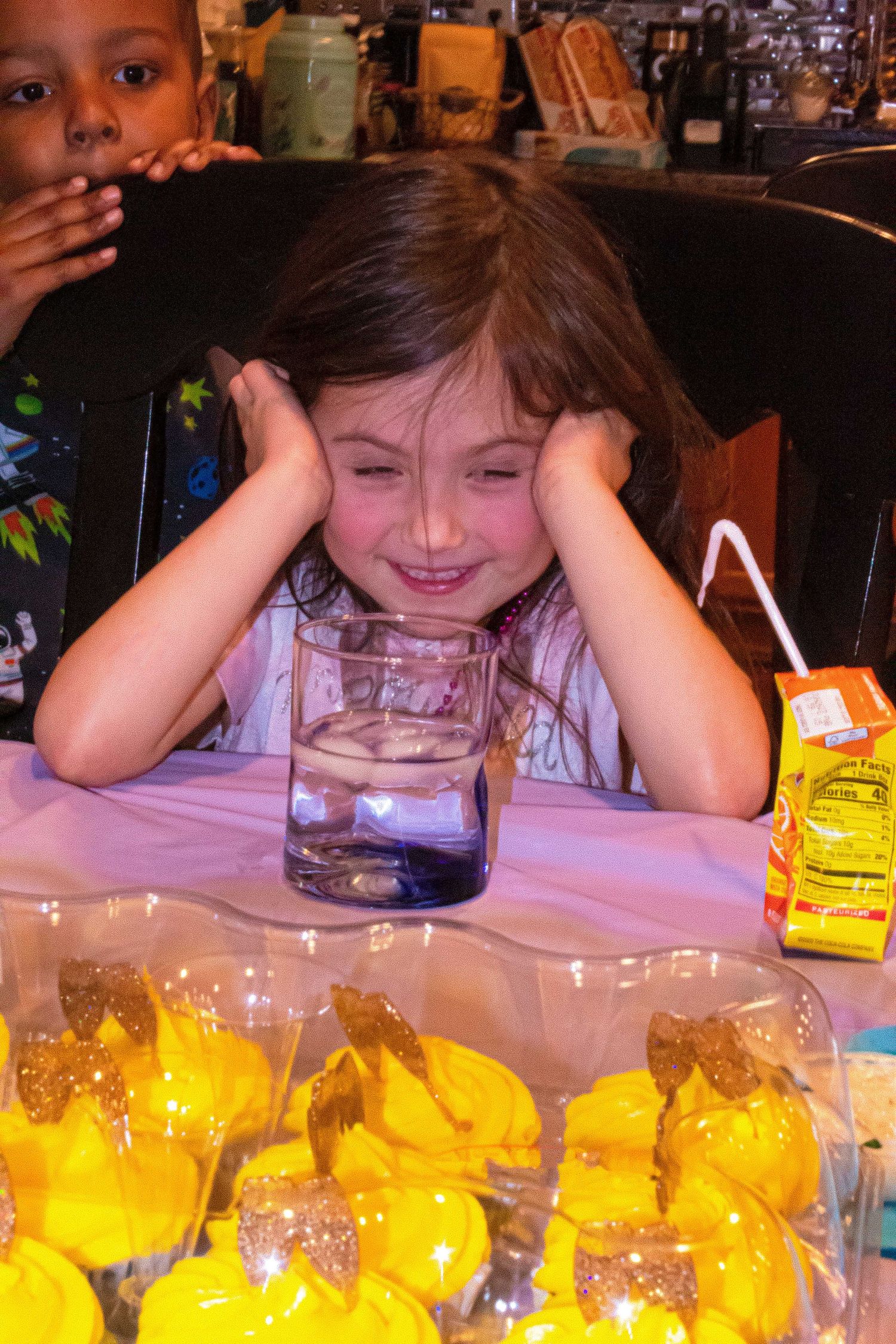 Top view of child leaning on table with yellow cupcakes.
