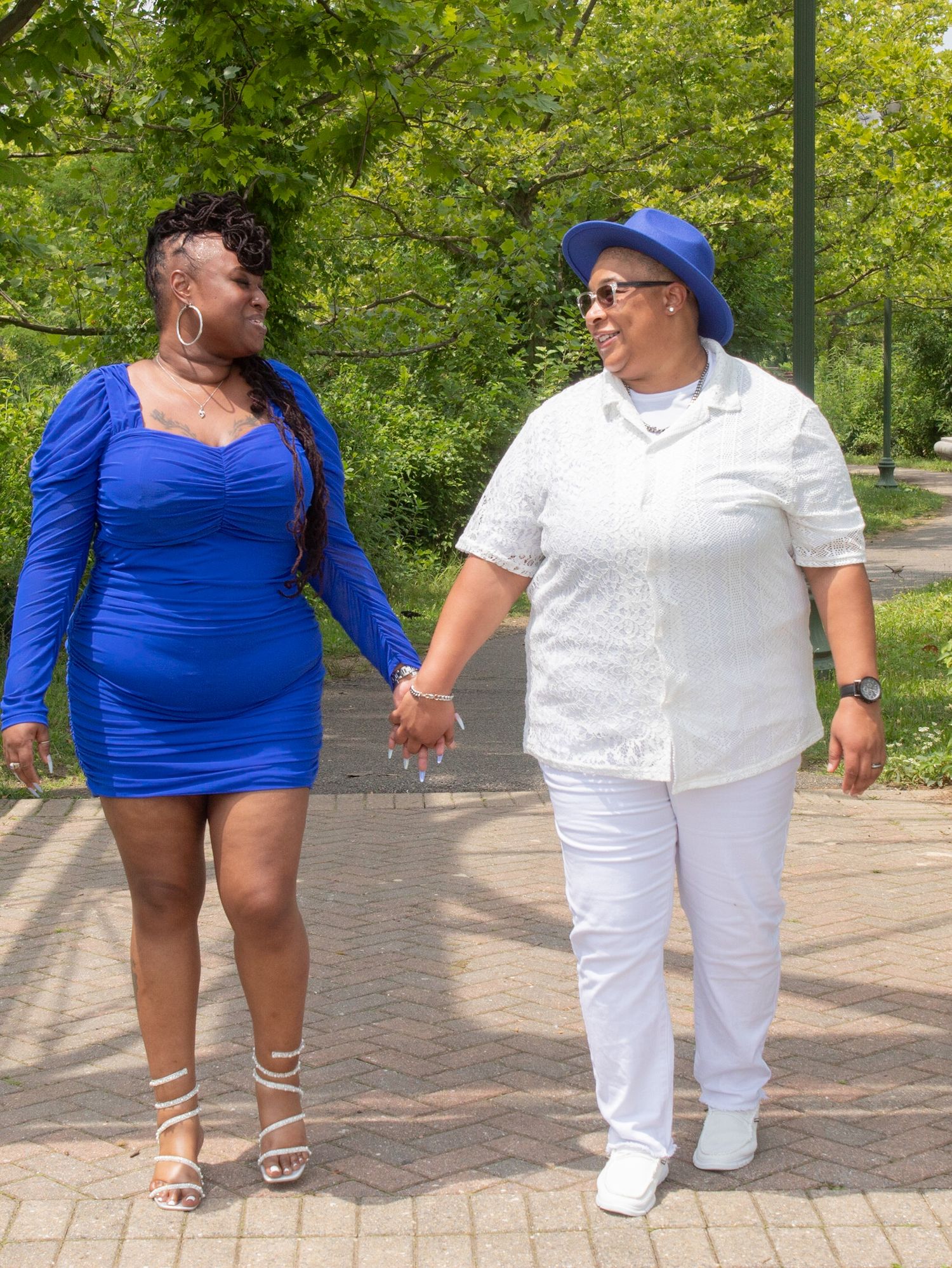 Couple holding hands while walking outdoors in coordinated blue and white outfits on a brick pathway.