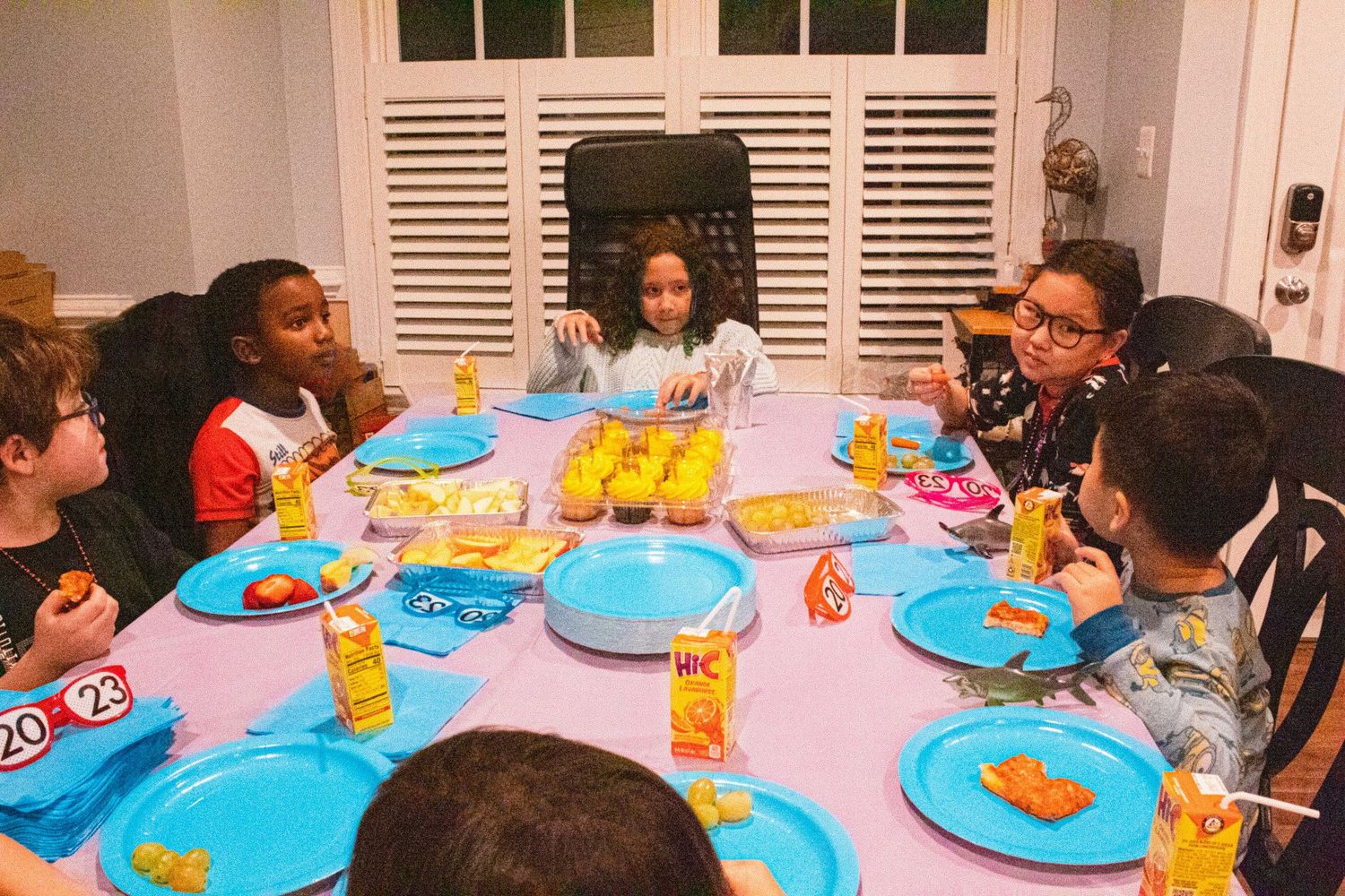 Young people gathered around a dining table with blue plates and yellow drinks for a party.