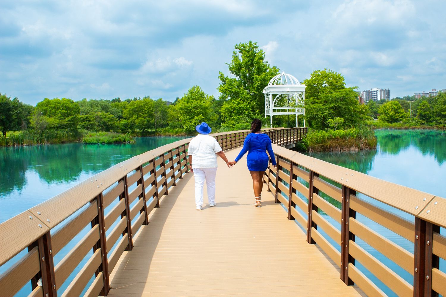 Scenic wooden boardwalk stretches across turquoise water on a sunny day with green trees in the background.