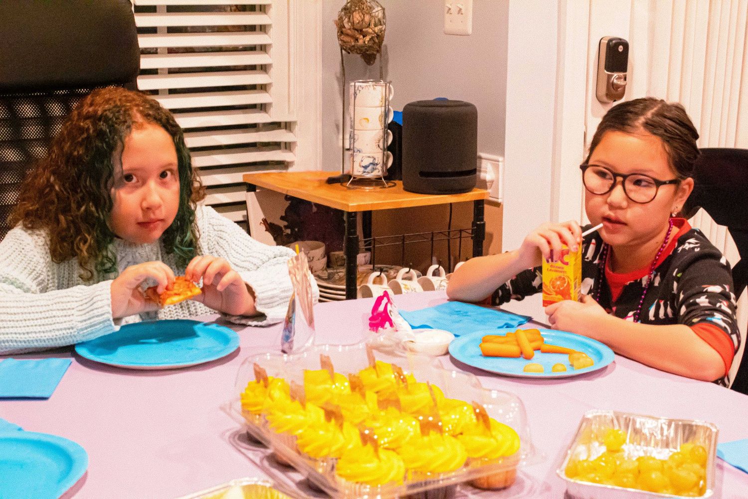 Two party guests enjoying refreshments at a table decorated with yellow cupcakes and blue plates.