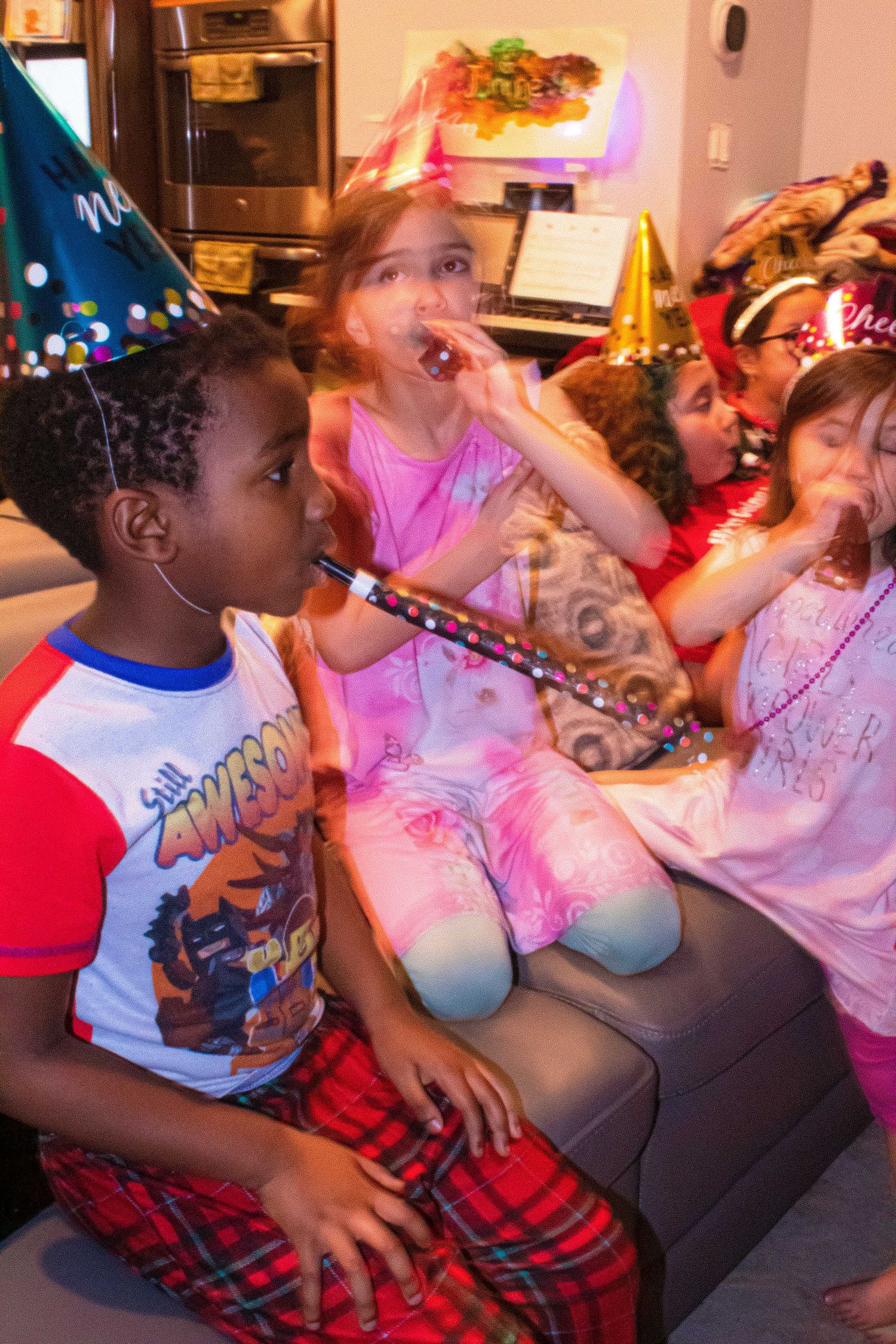 Children in party hats sitting on couch during celebration.