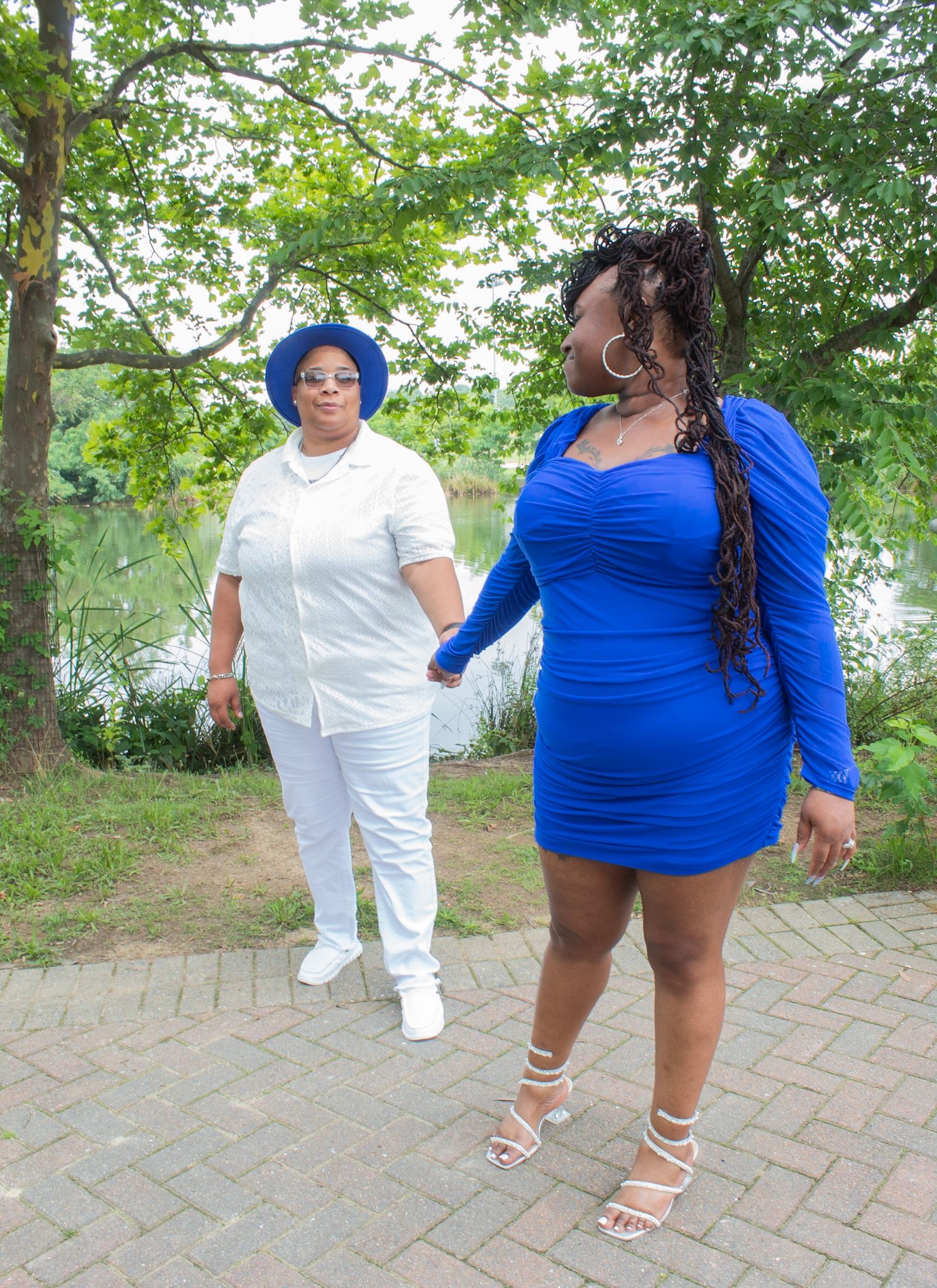 Two people in contrasting blue and white outfits walking on a brick pathway surrounded by greenery.