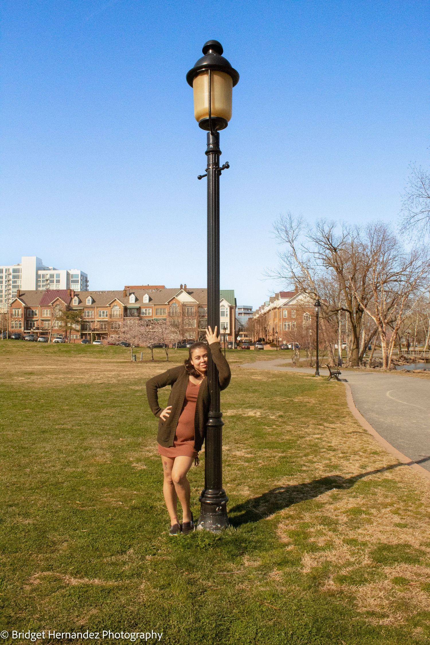 Playful poses against vintage lamppost in park setting with city buildings in background.