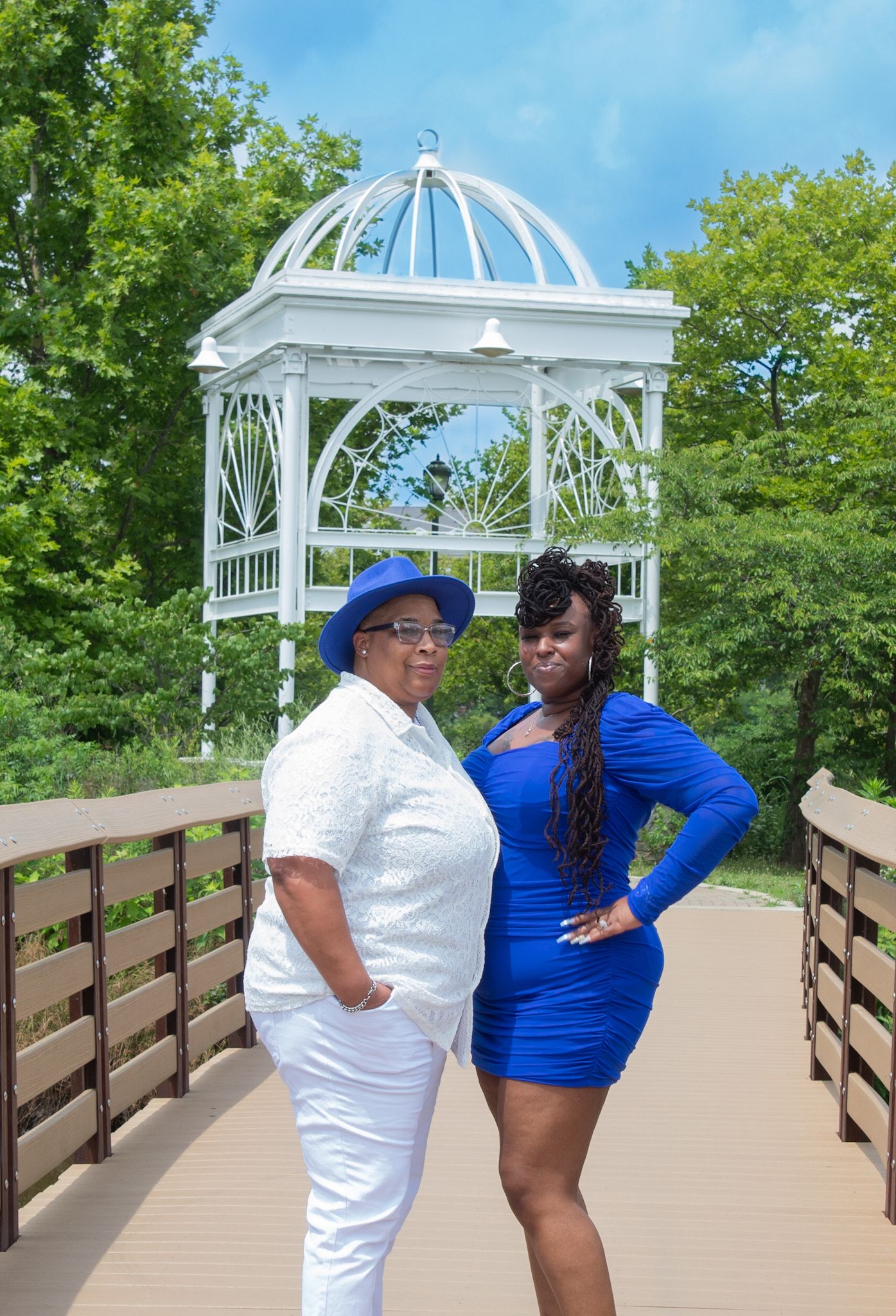 Couple poses under white gazebo on wooden boardwalk during maternity photoshoot.