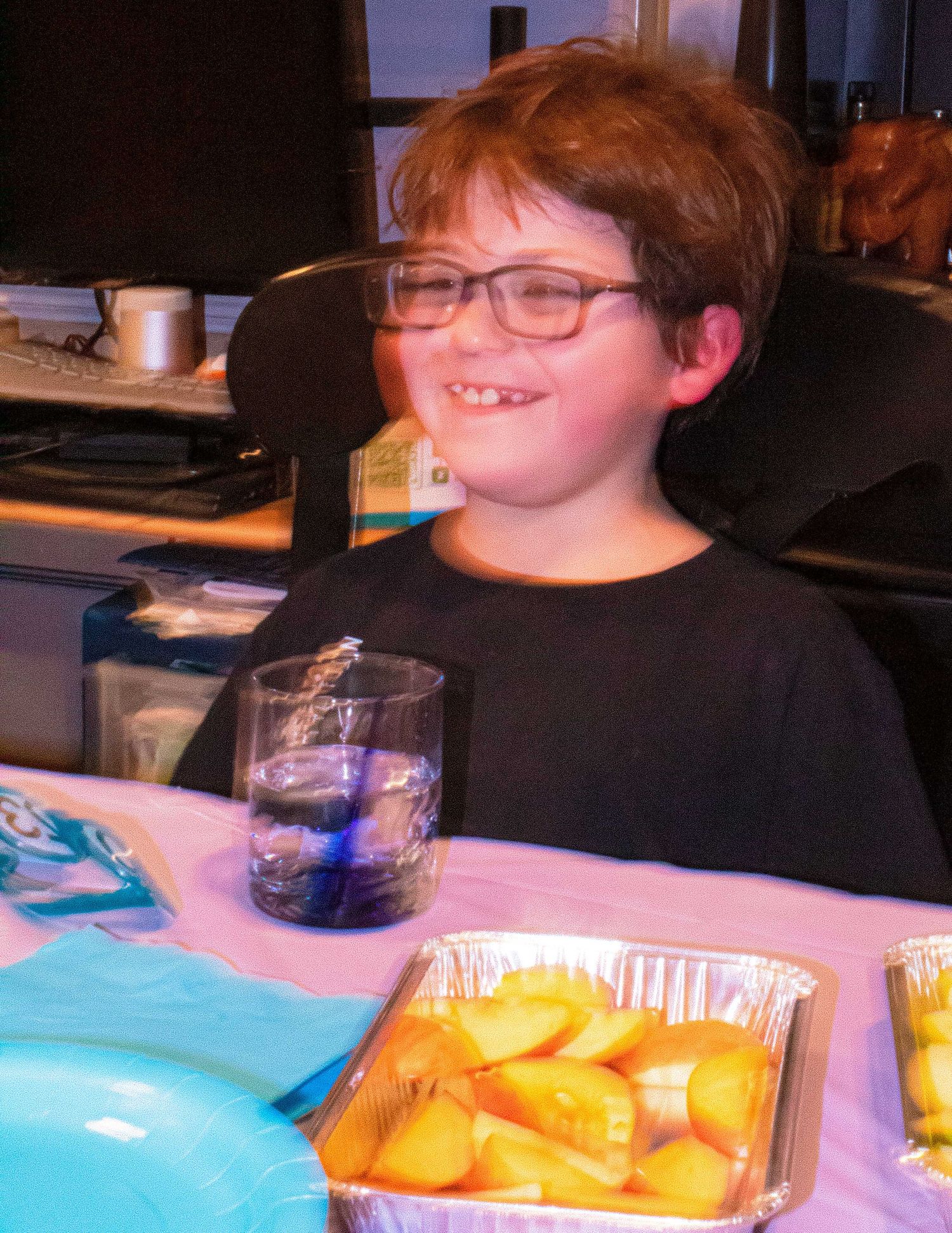 Young person in black shirt smiling while sitting at a party table with snacks.