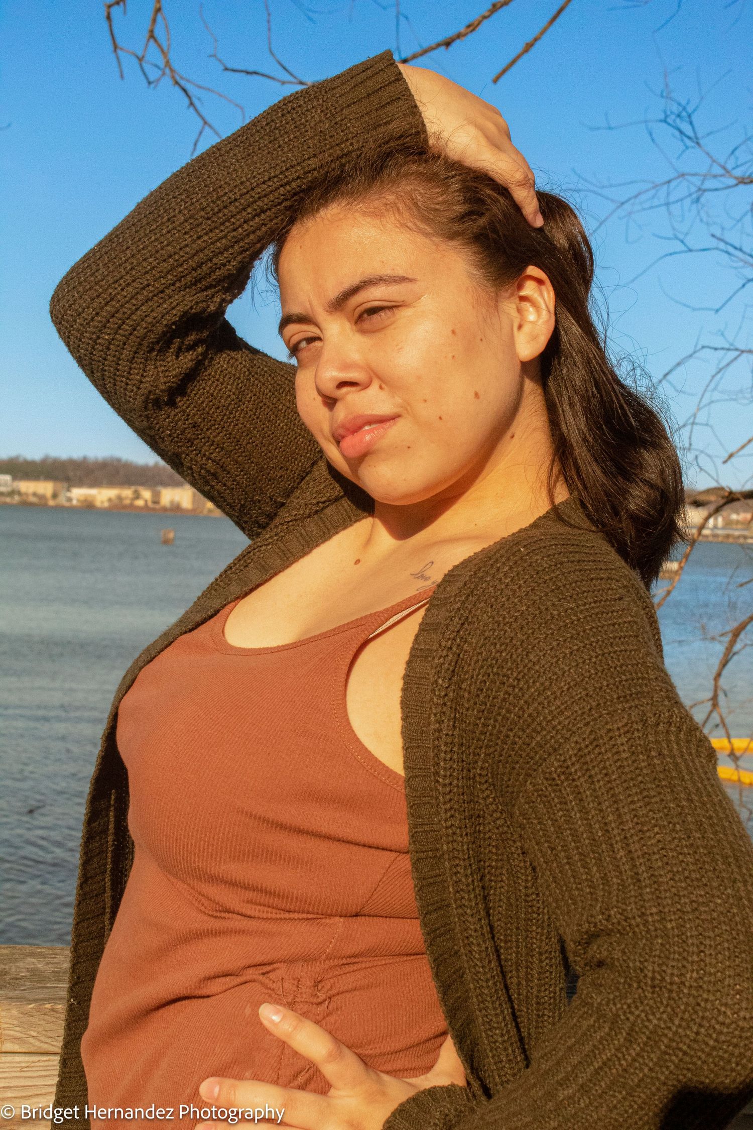 Woman in brown cardigan and orange dress enjoying golden hour by the water.