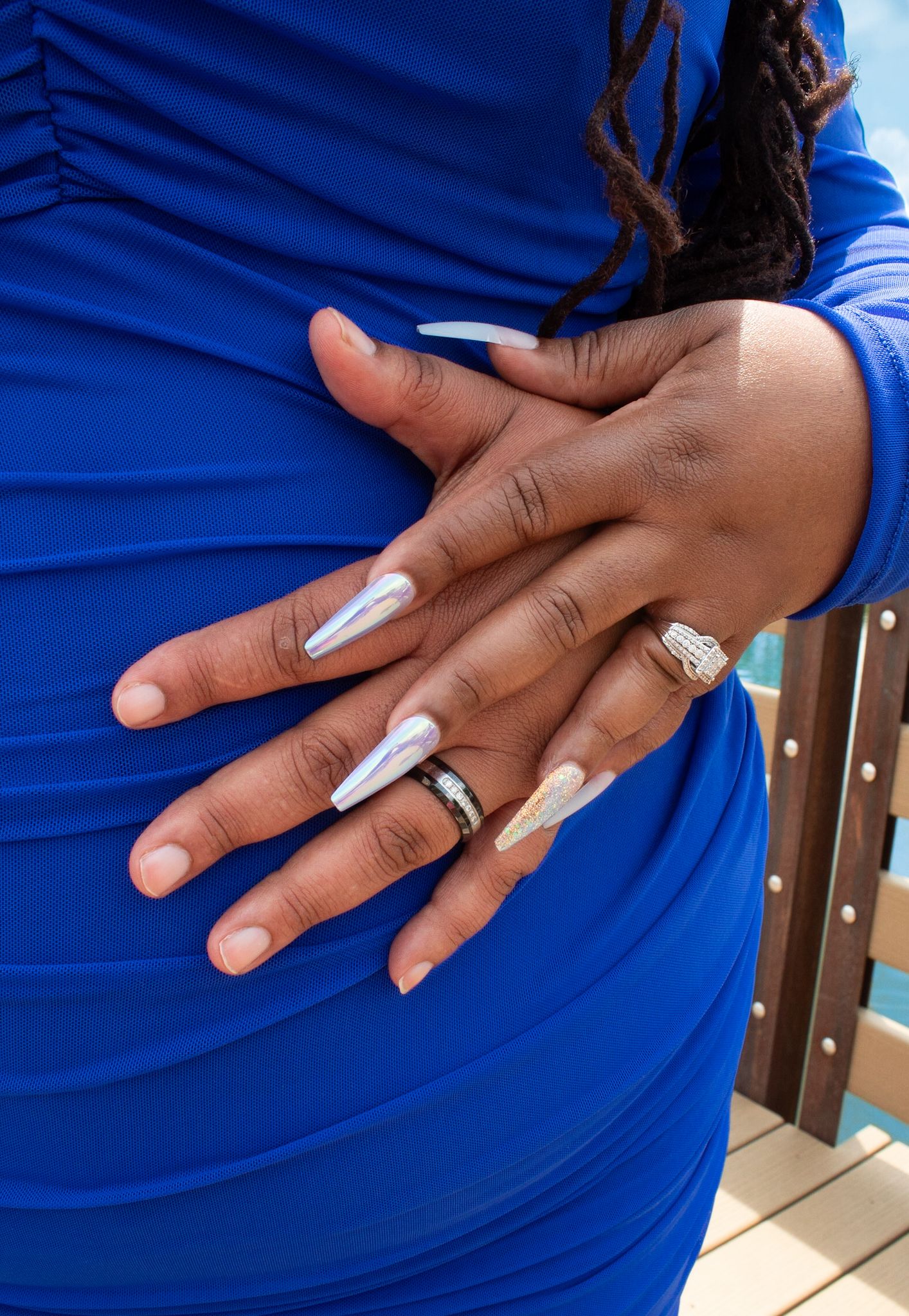 Close-up of hands resting on royal blue fabric showing elegant white manicure and jewelry.