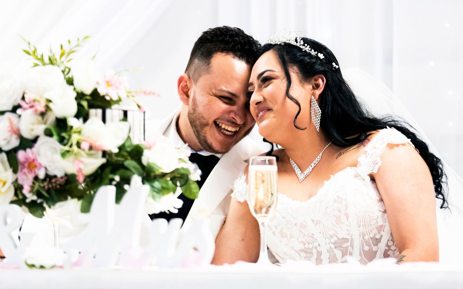 Bride and groom sharing joyful moment at wedding reception table with champagne and floral decor.