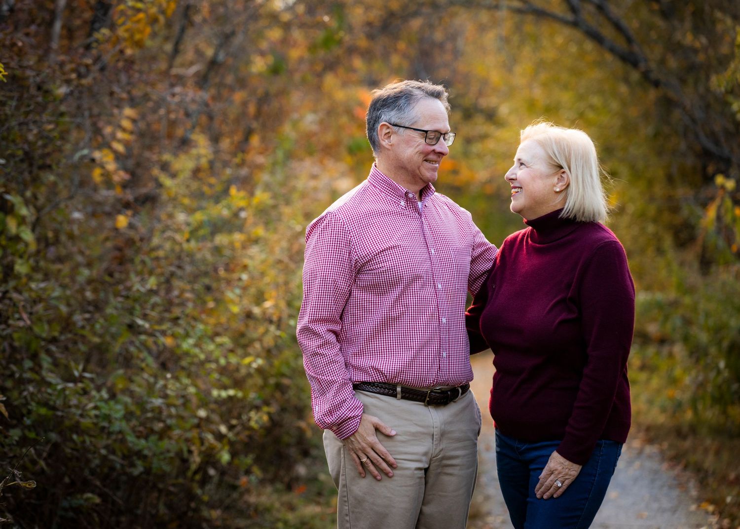 Smiling couple in coordinating pink and burgundy outfits standing together on an autumn path.