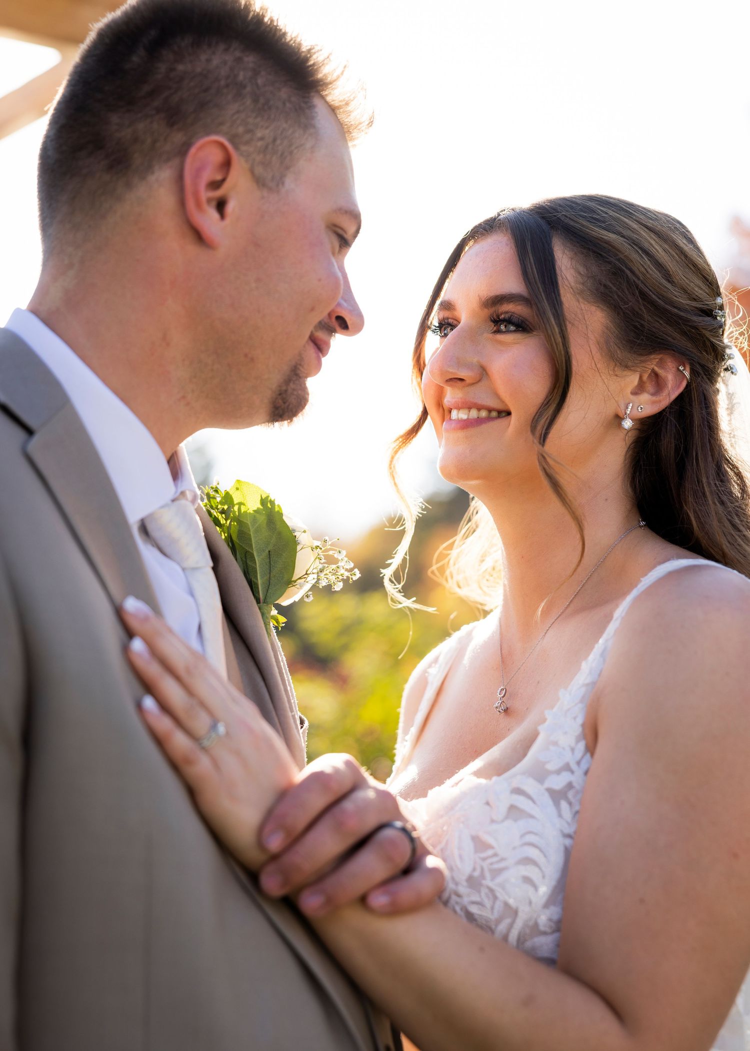 Bride gazes lovingly at groom in golden sunset light during outdoor wedding portrait.