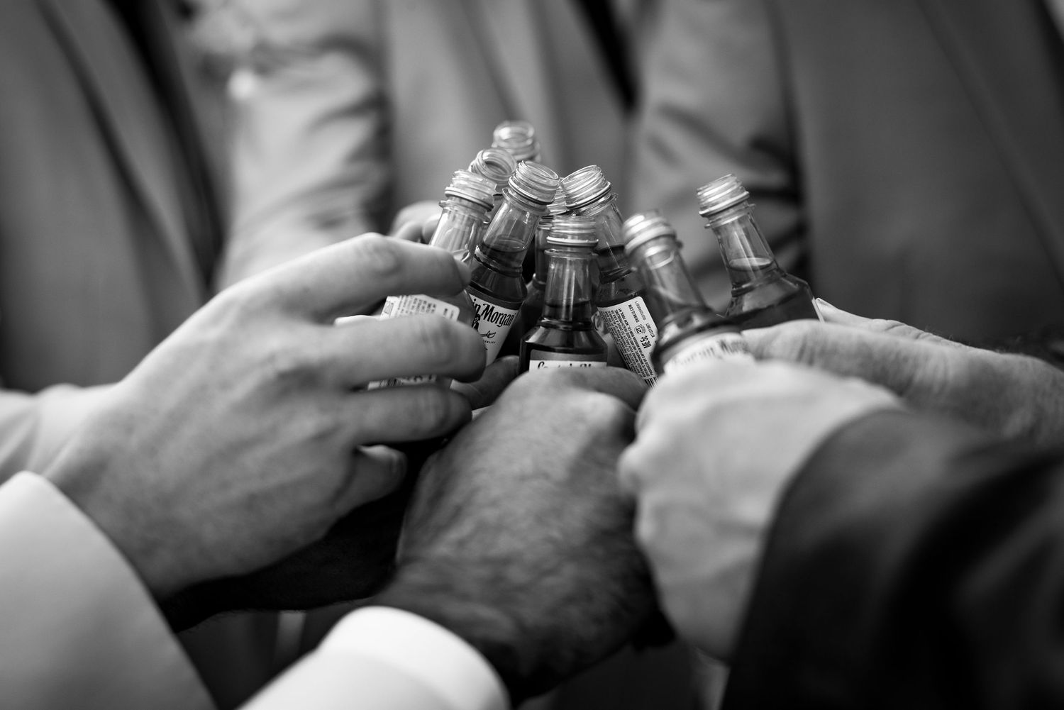 Black and white photo of groomsmen clinking small bottles together in a celebratory wedding day toast.