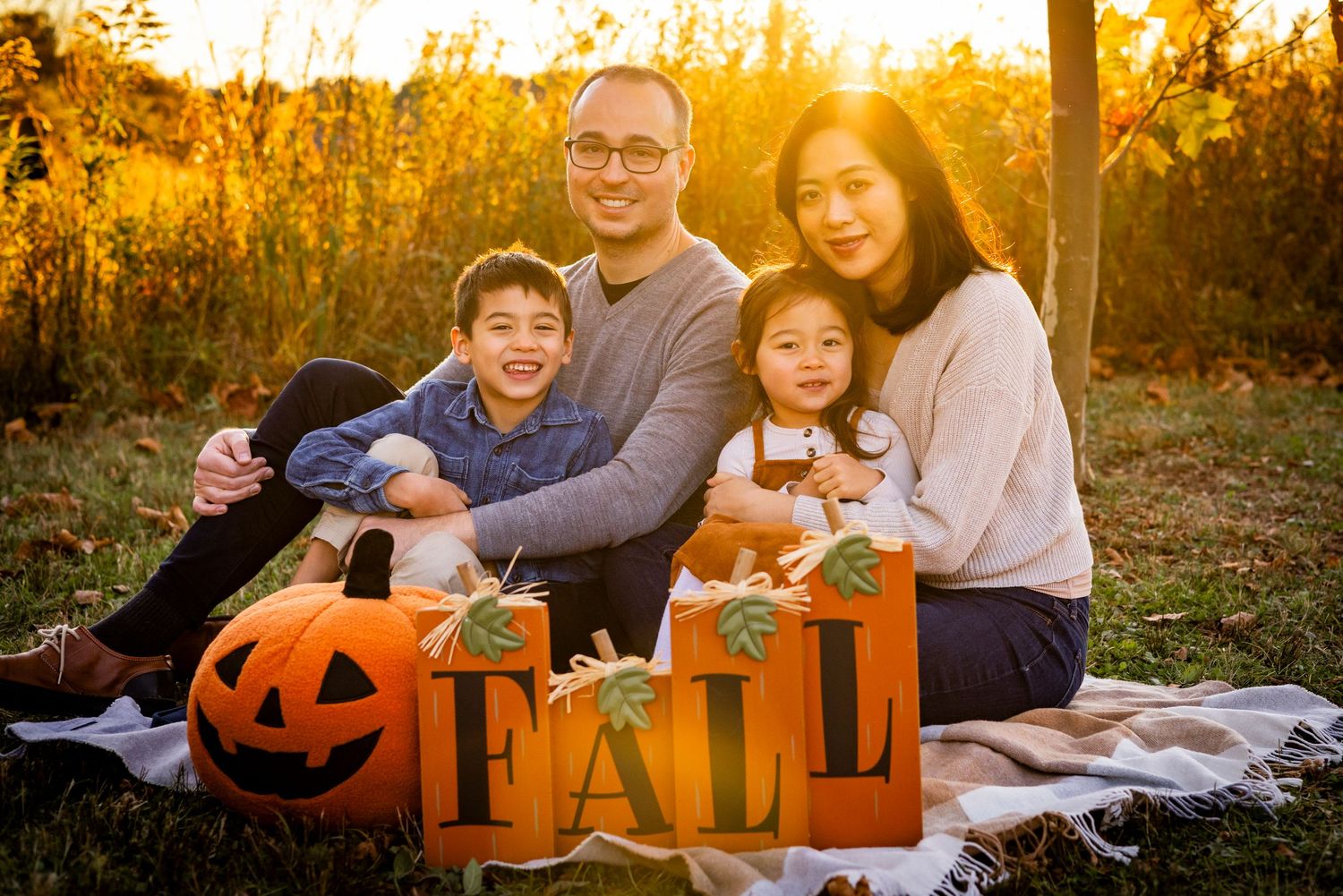 A happy family of four poses with fall pumpkins and FALL signs during a golden autumn photo session.