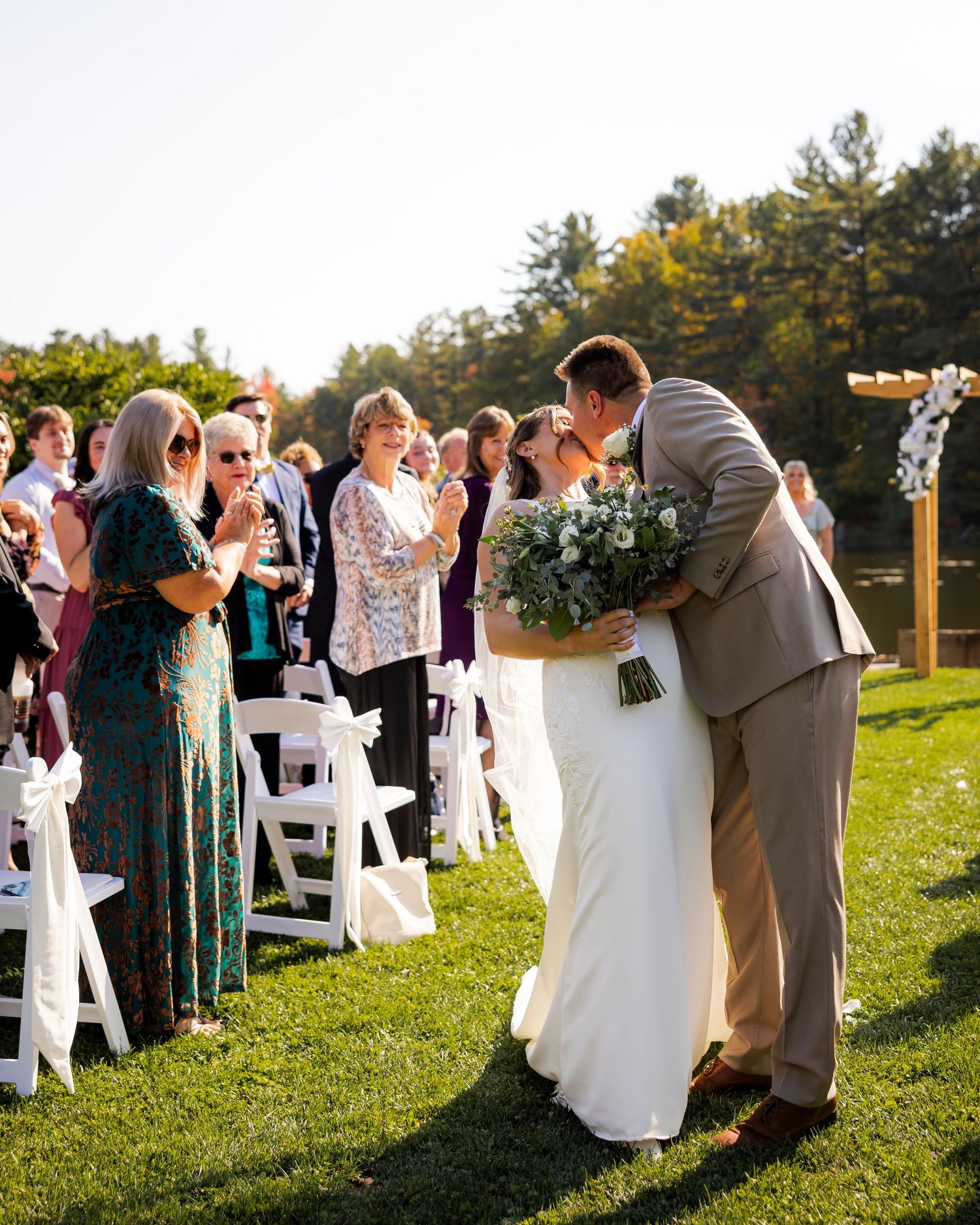 Newlyweds share a tender kiss while walking down the aisle at an outdoor wedding ceremony.