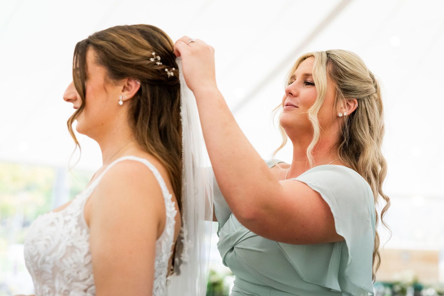Bridesmaid carefully adjusts bride's veil and hair before the wedding ceremony.