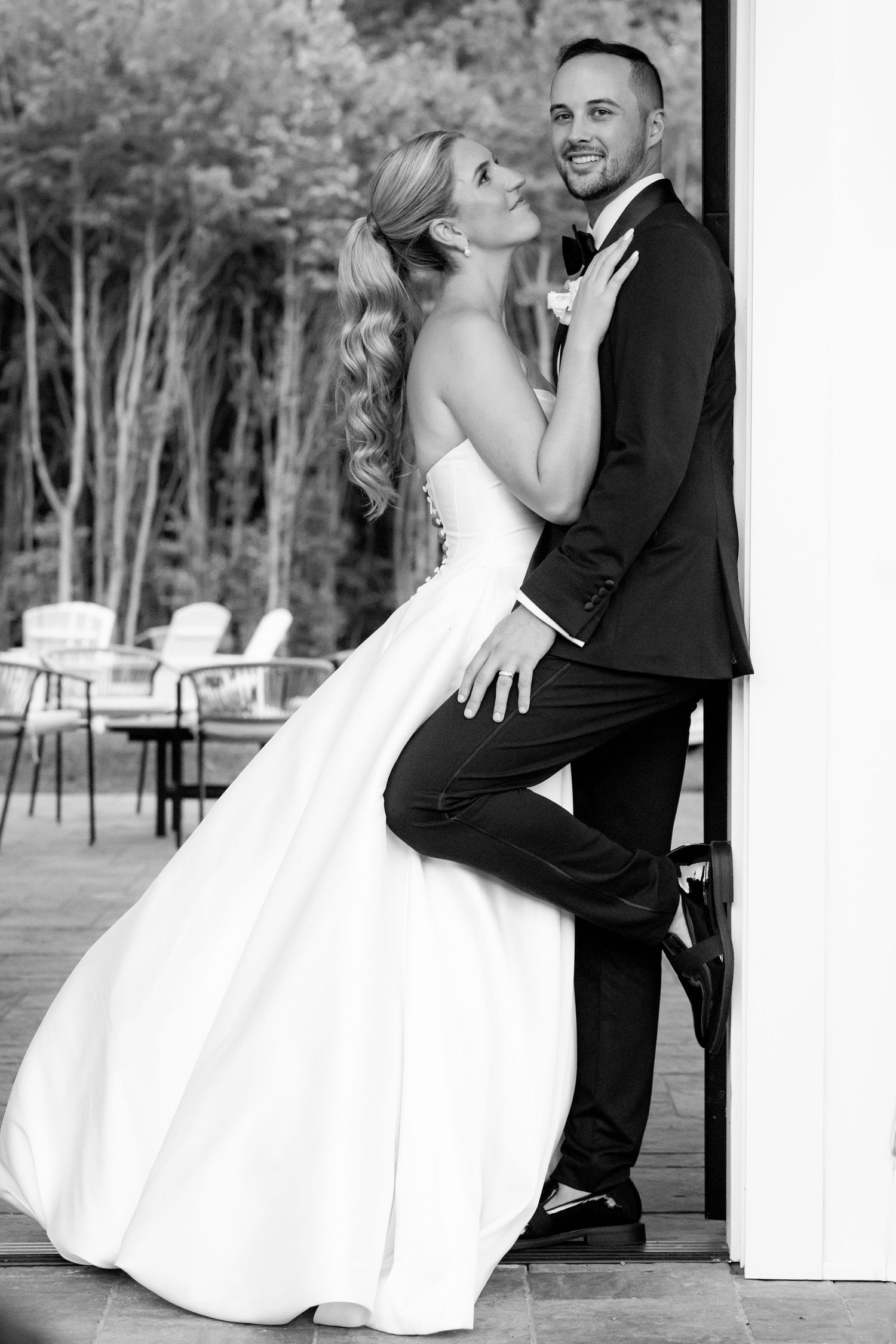 Bride and groom pose playfully in black and white photo, leaning against doorway at venue.