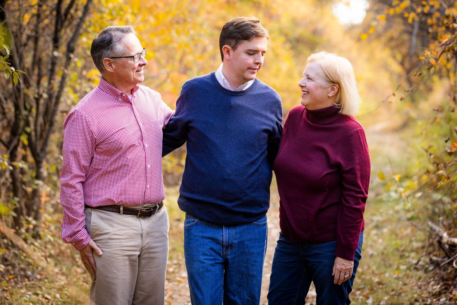 Family of three walking on an autumn trail, parents proudly flanking their teenage son.