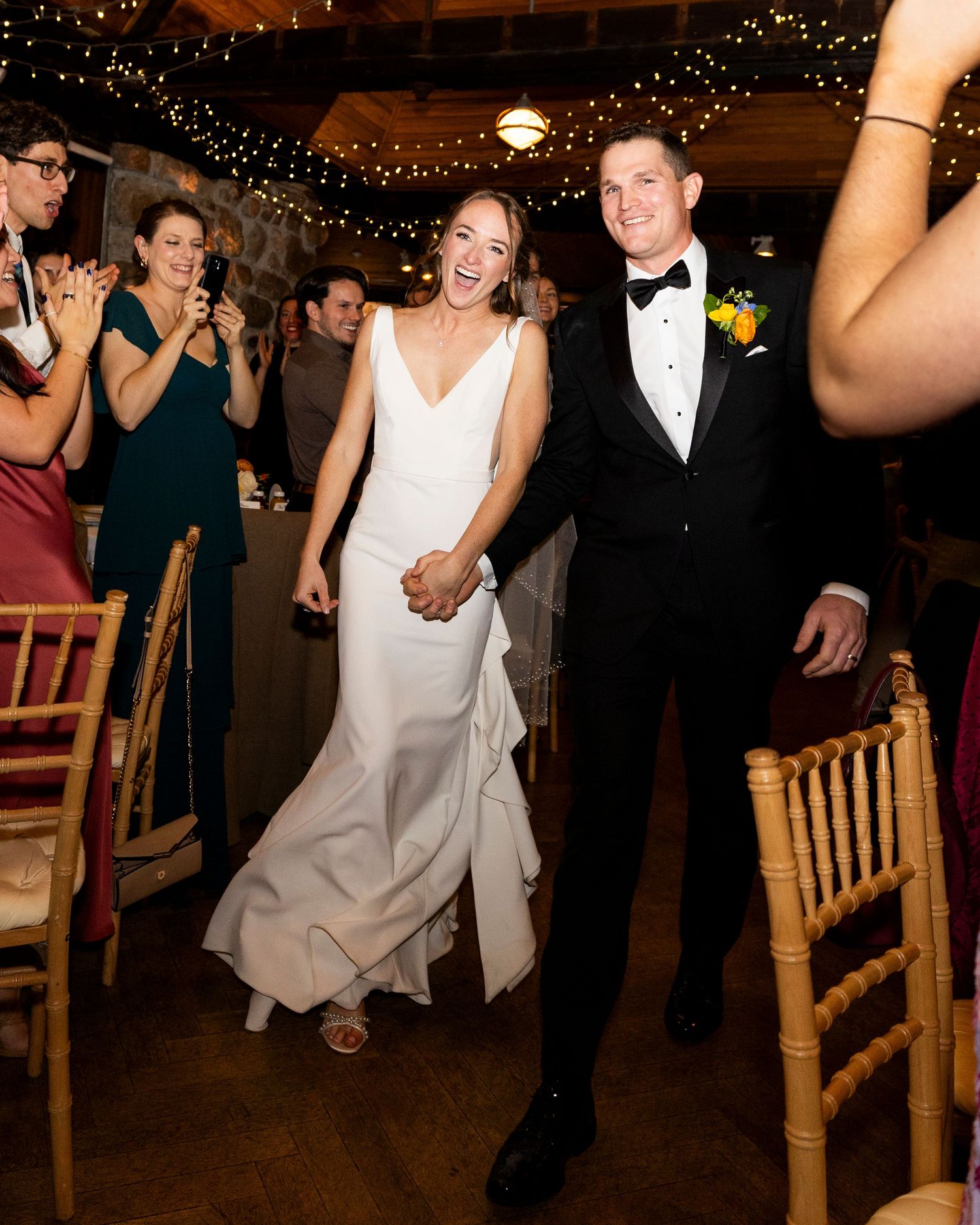 Laughing bride in white gown and groom in tuxedo making grand reception entrance.